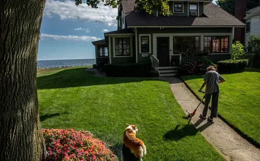 Nancy Sullivan, with dog Carter, tends to her house along the shore of Lake Ontario in Greece, New York, on July 30, 2020. She has lived at this house for the past 55 years and recently spent some of her retirement money to repair her seawall. Image by Zbigniew Bzdak/Chicago Tribune. United States, 2020.