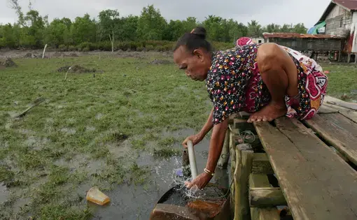 A woman crouches over to pump water.