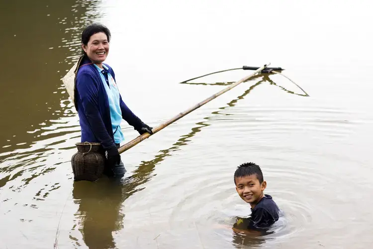 Phetsamay fishes in a style unique to her region while her son plays next to her. Image by Erin McGoff. Laos, 2017.