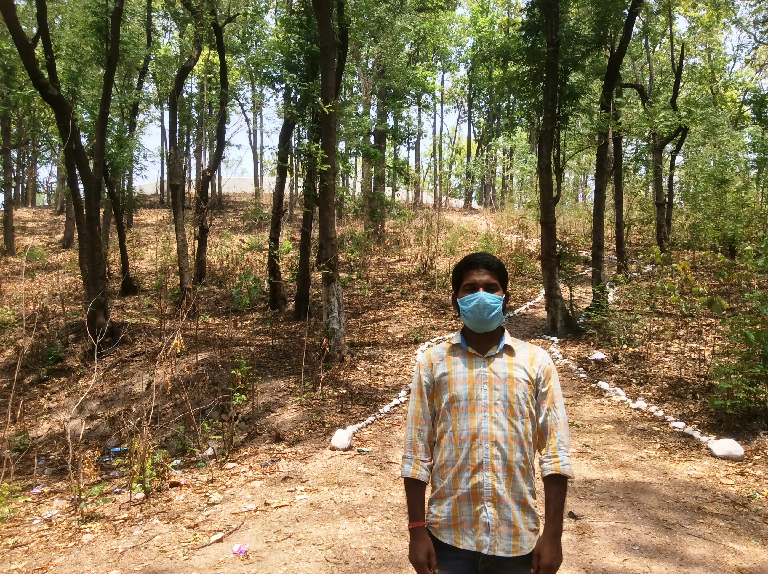 Man stands masked in a forest in his village