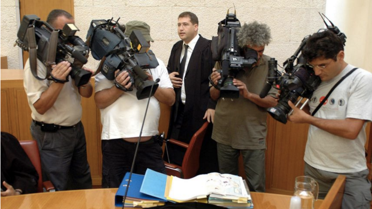 Israeli human rights lawyer Michael Sfard stands in court while reporters film documents on a desk. Image by Tomer Appelbaum. Israel.