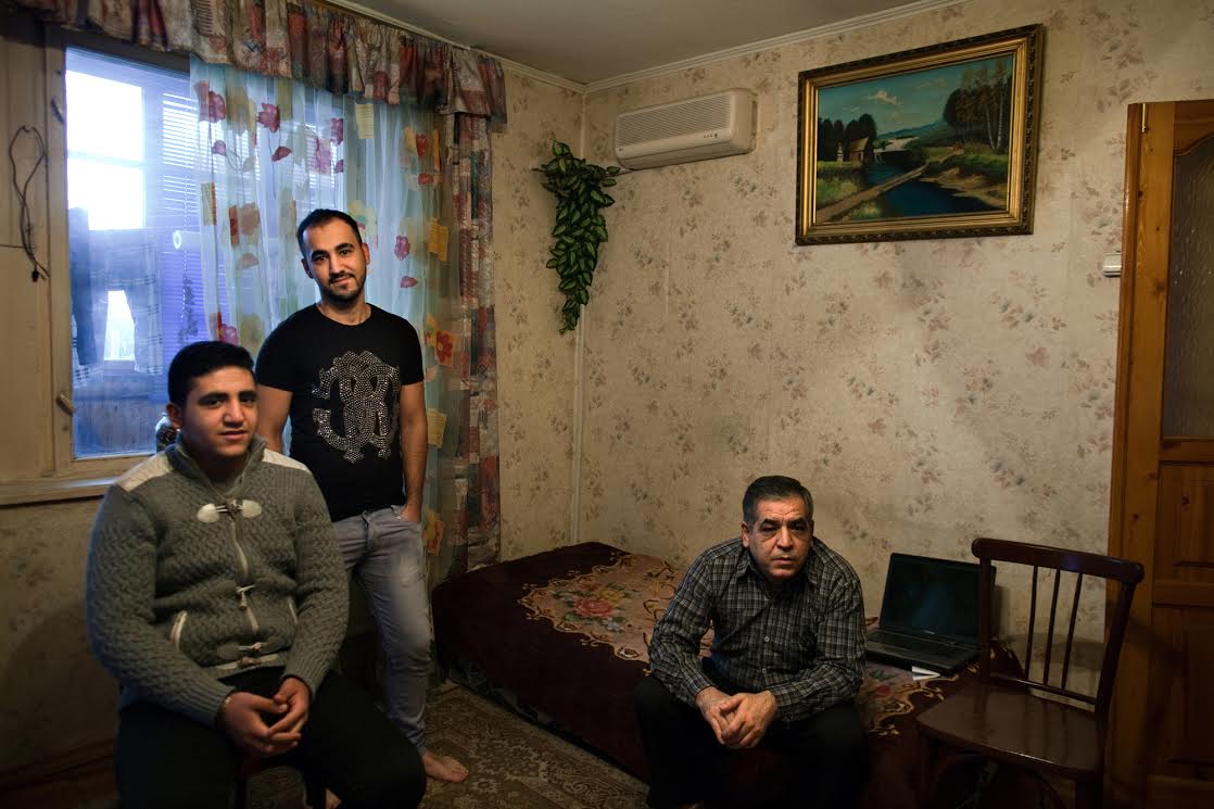 Yasser, center, a 23-year-old Syrian refugee, at his home with his brother Ahmed, 16, left, and father Abu Yasser, right, in Noginsk, Russia, Nov. 14, 2014. Yasser came to Noginsk with his father in 2008 to work as a tailor in one of the Syrian-operated textile factories in this town just outside of Moscow. The rest of Yasser's family came after the conflict in Syria started in 2011, and his family's home in the neighborhood of Salahadin in Aleppo was destroyed by shelling in 2012. Now Yasser and his family are stuck here, with little support and no hope of asylum. Image by Holly Pickett. Russia, 2014. Media file: unnamed.jpg