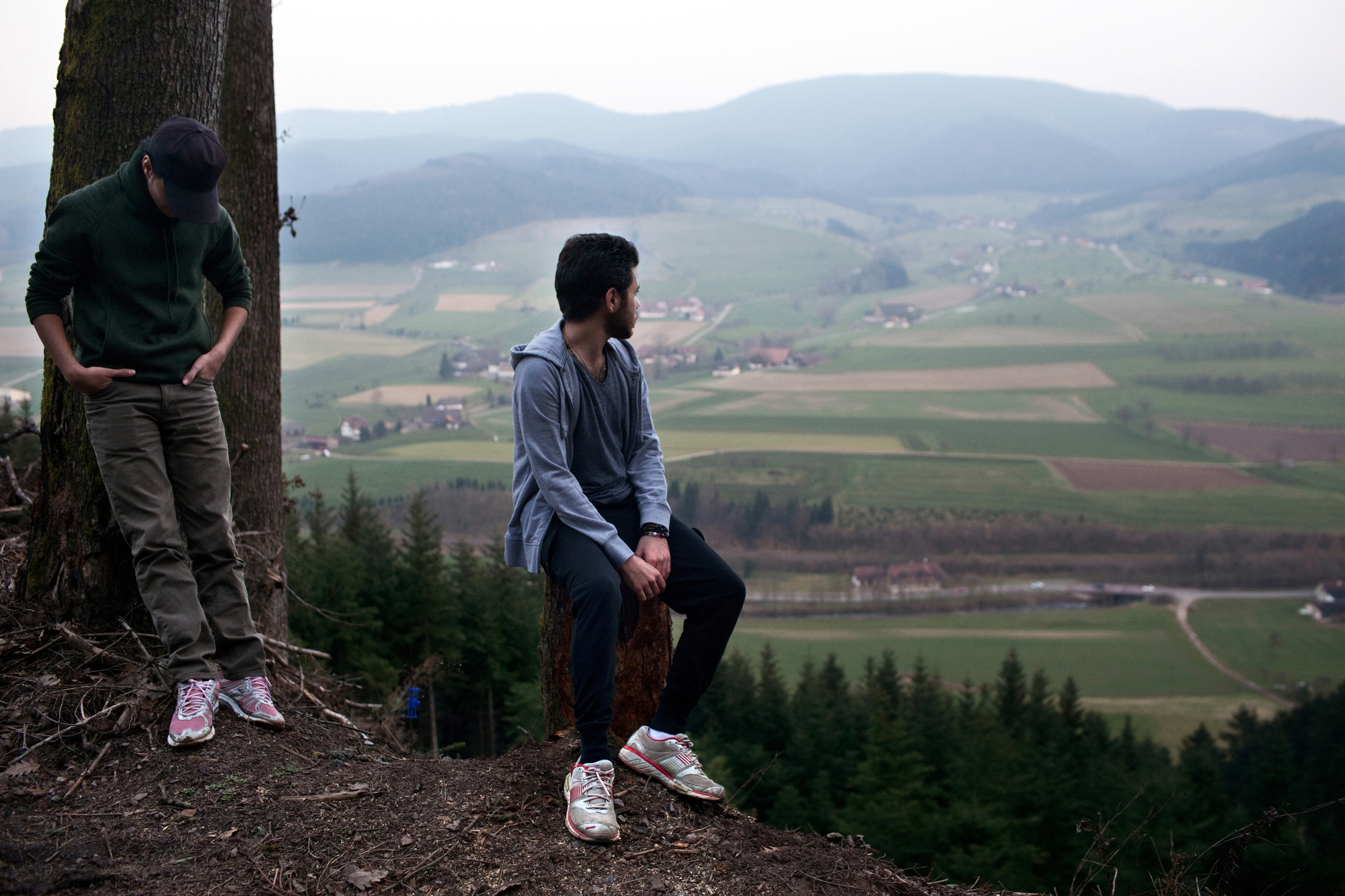 Rafat Al Aydi, 20, right, takes in the view of southwestern Germany with his brother Naif, 16, during a walk in the Black Forest near their home in tiny Zell am Hammersbach, Germany in March 2014. The four Al Aydi boys, unable yet to speak German, struggled to adjust to life in their new village, but it wasn’t long before their family was on the move again, searching for a real place to call home. Image by Holly Pickett. Germany, 2014.