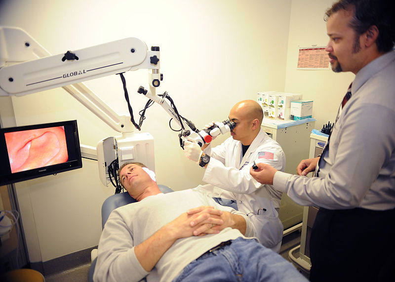 Lt. Art Ambrosio, center, a second-year resident in the Otolaryngology Department at Naval Medical Center San Diego, and Ear, Nose and Throat technician Zapata Hough examine the left ear of Christopher Donoho. Image by Joseph A. Boomhower / U.S. Navy. United States, 2011.