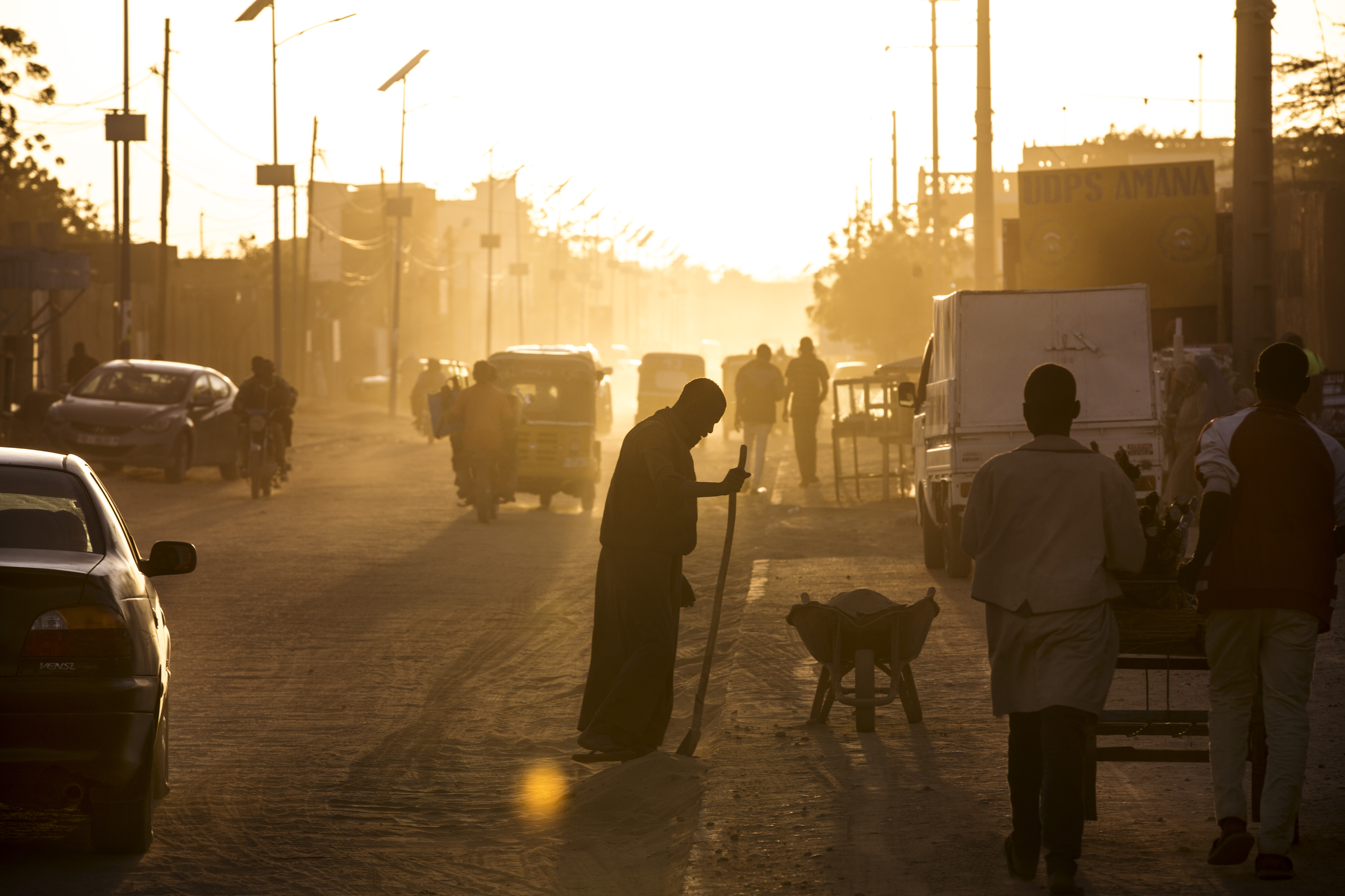 A man sweeps dust off the street at dusk in Agadez, Niger, January 16, 2018. Image by Joe Penney. Niger, 2018. A man sweeps dust off the street at dusk in Agadez, Niger, January 16, 2018. Image by Joe Penney. Niger, 2018.