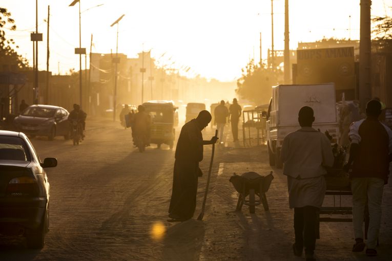 A man sweeps dust off the street at dusk in Agadez, Niger, January 16, 2018. Image by Joe Penney. Niger, 2018. A man sweeps dust off the street at dusk in Agadez, Niger, January 16, 2018. Image by Joe Penney. Niger, 2018.