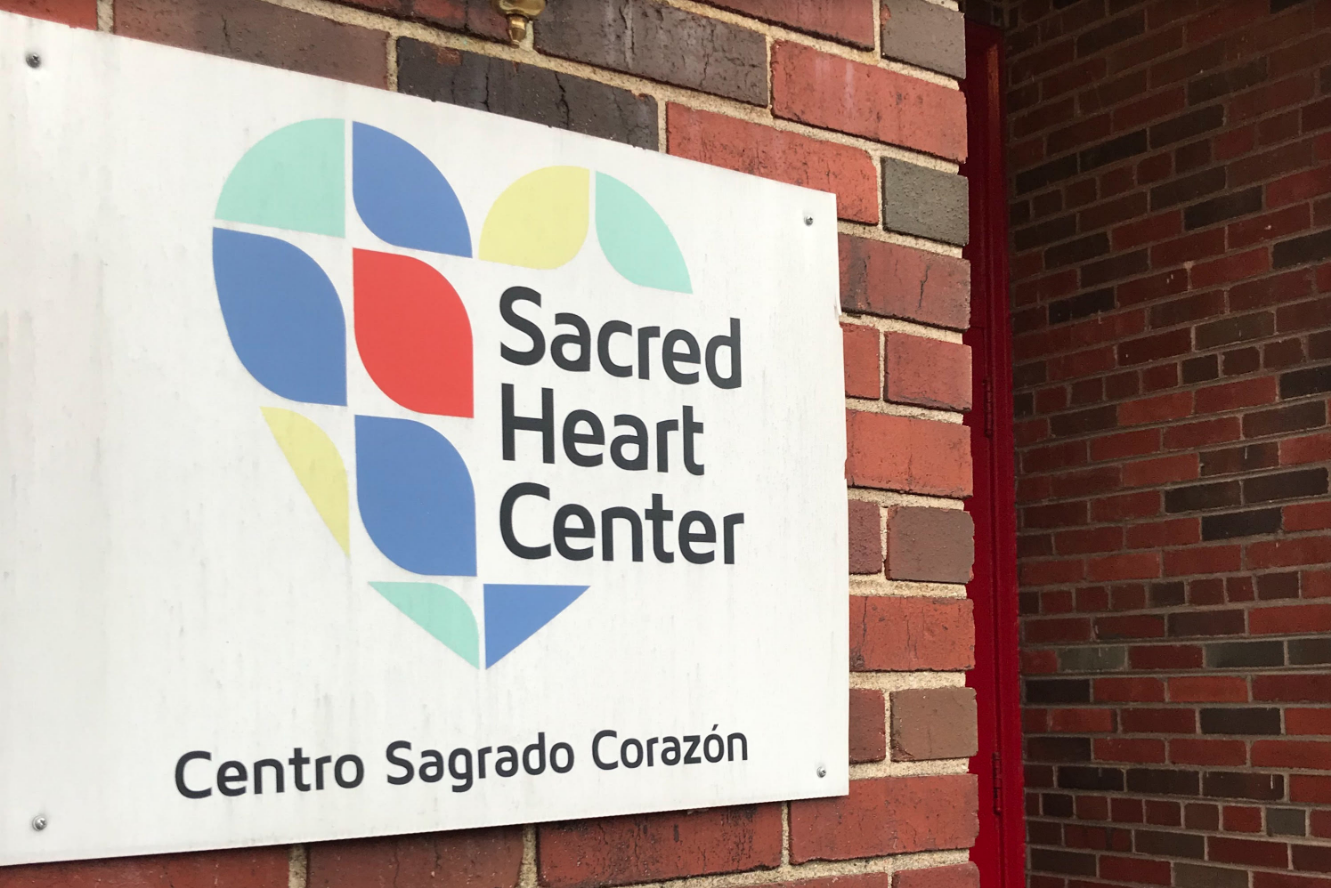 A bilingual sign at the Sacred Heart Center, welcoming all those who enter the community building. Image by Jack Sims. United States, 2019. A bilingual sign at the Sacred Heart Center, welcoming all those who enter the community building. Image by Jack Sims. United States, 2019.