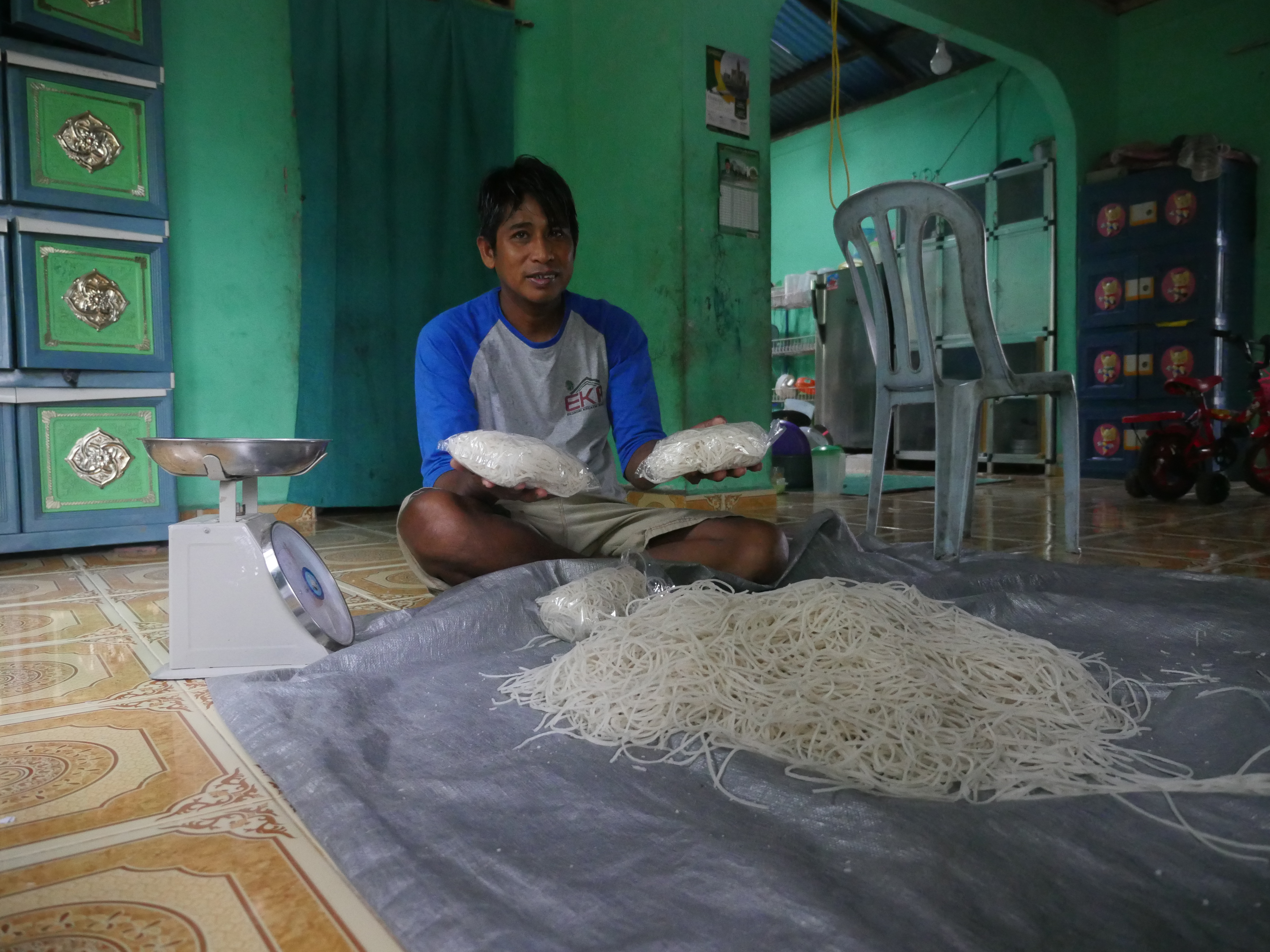 Abdul Manan makes sago noodles with a small pasta maker and packs them for retail sale in plastic bags. He sells about one ton of pasta each month. Image by Daniel Grossman. Indonesia, 2019. Abdul Manan makes sago noodles with a small pasta maker and packs them for retail sale in plastic bags. He sells about one ton of pasta each month. Image by Daniel Grossman. Indonesia, 2019.