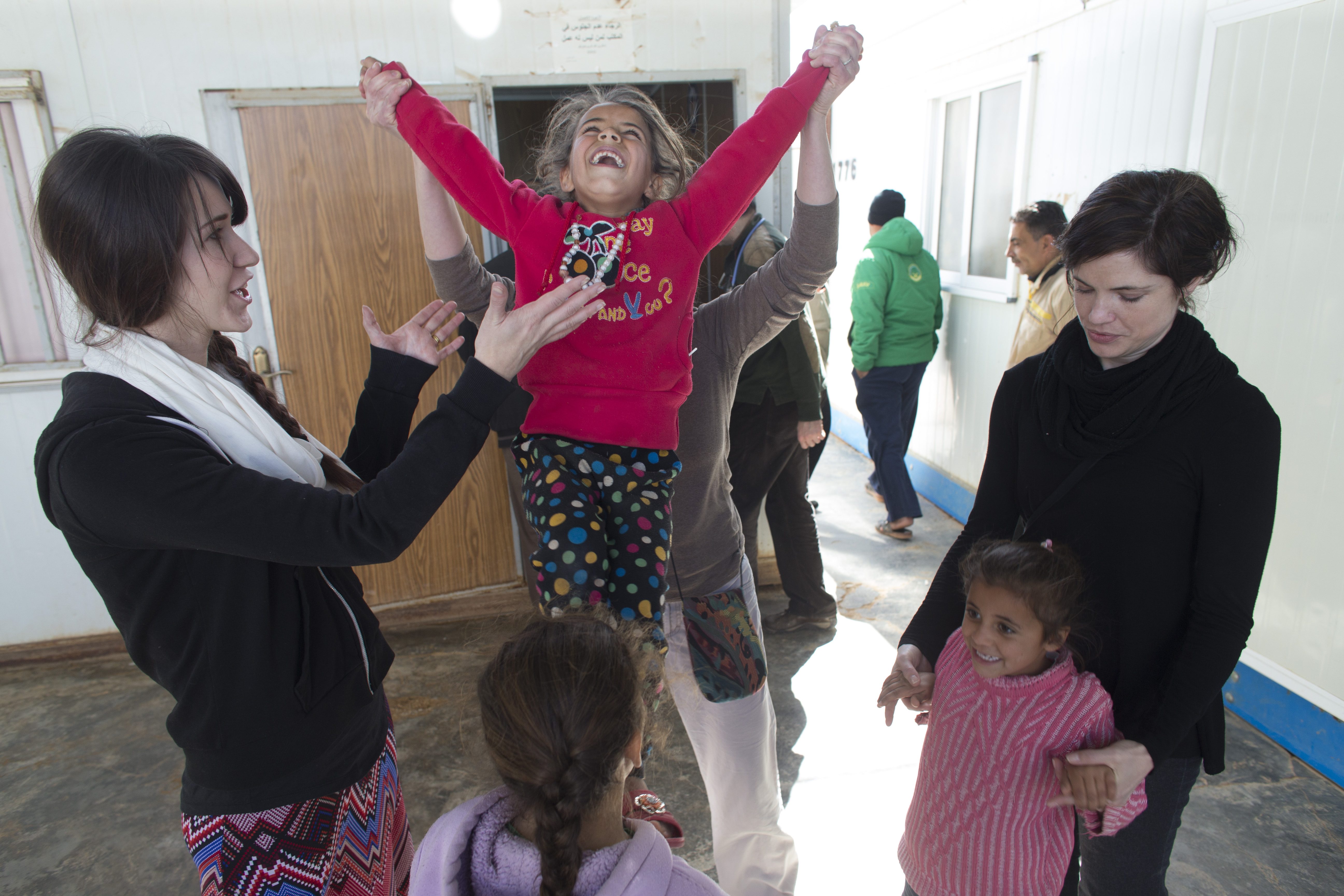 Social worker Stacey Volkman launches a girl into the air while playing with children along with Jennifer Nitschke-Thomas (left) and JoAnna Balza (right) Sunday, March 20, 2016 at the Zaatari refugee camp in Jordan about 15 miles from the Syrian border. Image by Mark Hoffman. Jordan, 2016.