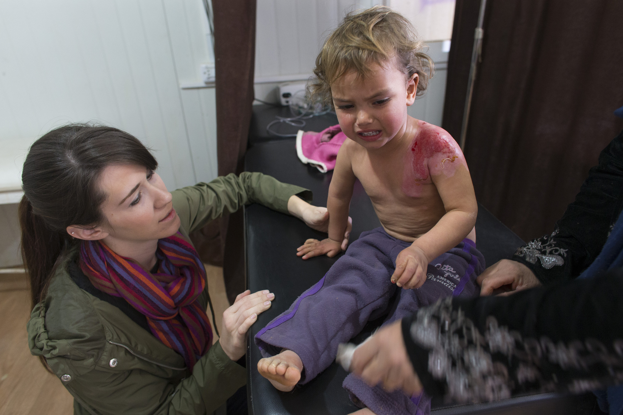 Rimaz, 2, is comforted by nurse Jennifer Nitschke-Thomas while her second-degree burns are treated at the Zaatari Refugee Camp. Image by Mark Hoffman. Jordan, 2016. Media file: jordan_trip_2.jpg