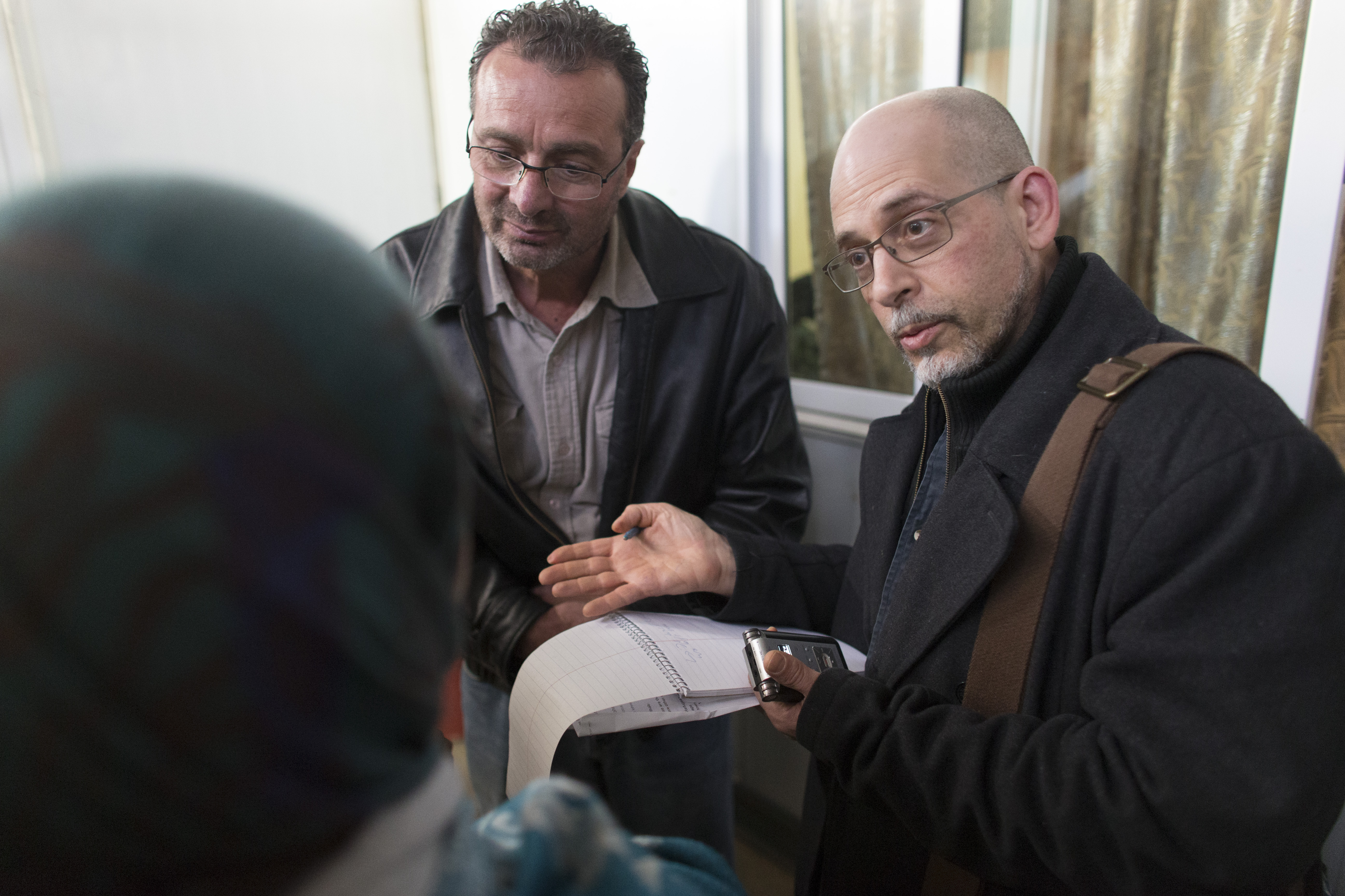 Reporter Mark Johnson (right) and translator Ihab Muhtaseb talk with clinic patients Sunday, March 20, 2016 at the Zaatari refugee camp in Jordan about 15 miles from the Syrian border. Brookfield pediatric neurologist Tarif Bakdash is leading a medical mission from Milwaukee to the Zaatari refugee camp that is home to about 80,000 Syrians who have fled the five-year-old civil war in their country. Bakdash is a 51-year-old pediatric neurologist who grew up in Syria and worked at Children's Hospital of Wisconsin and the Medical College of Wisconsin. He recently quit his position there so he can find a job that would him more time off for relief work. Image by Mark Hoffman. Jordan, 2016. Media file: jordan_mark_johnson_3.jpg