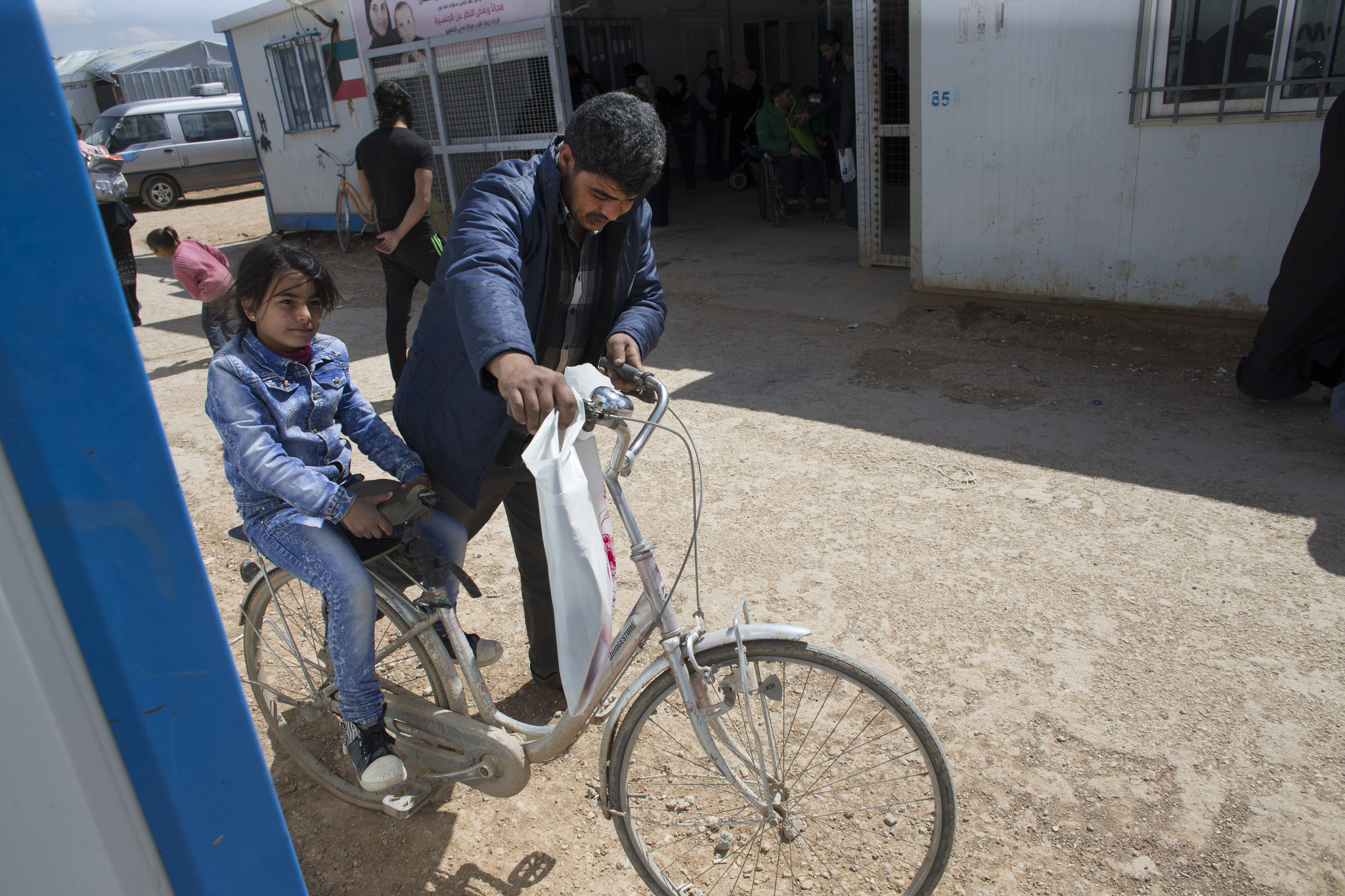 Mahmood Al Mekdad gets on his bike to take his 8-year-old daughter, Sandy, back to their home at the Zaatari refuge camp in Jordan. Image by Mark Hoffman. Jordan, 2016. Media file: jordan5.jpg