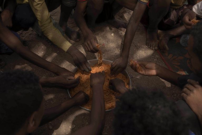 Ethiopian migrants eat spaghetti as they take shelter under a tree, in Obock, Djibouti. Image by AP Photo/Nariman El-Mofty. Djibouti, 2020. Ethiopian migrants eat spaghetti as they take shelter under a tree, in Obock, Djibouti. Image by AP Photo/Nariman El-Mofty. Djibouti, 2020.