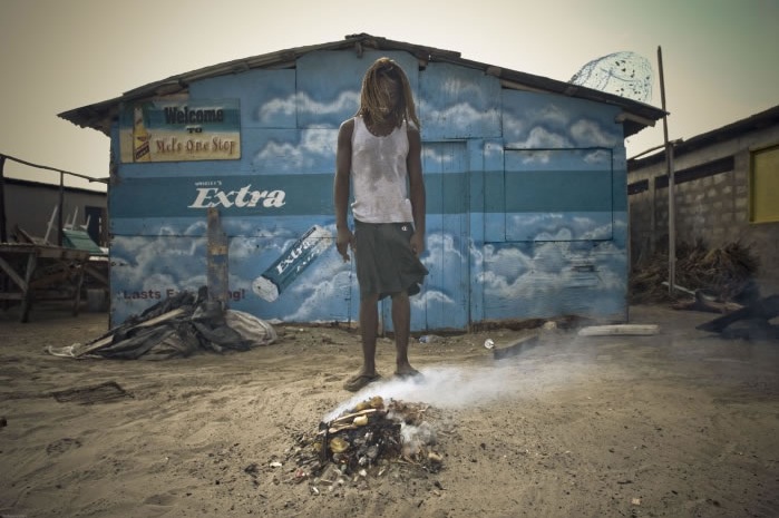 A boy warms himself in the morning in front of a pile of burning trash in Portmore. Image by Joshua Cogan. Jamaica, 2008. Media file: lhl.jpg