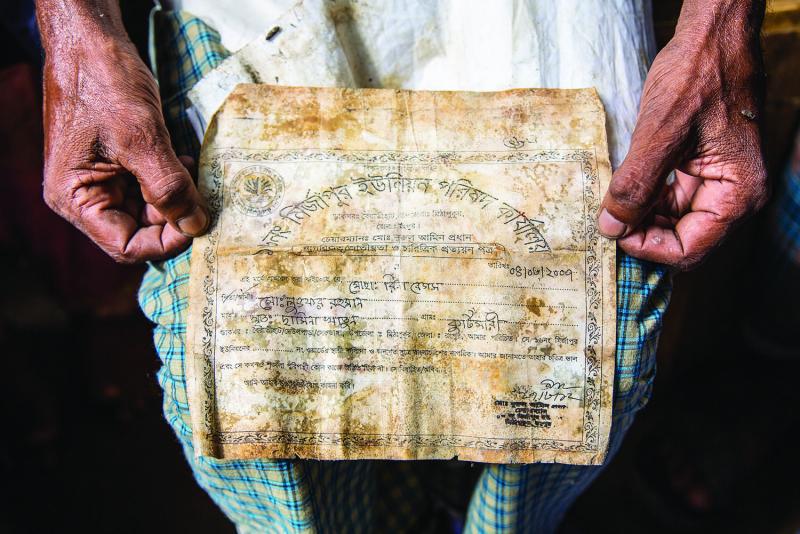Lutfer Rahman holds the document that his daughter found next to the body of his wife, Rina Rahman, confirming her death in the collapse. Image by Jason Motlagh. Bangladesh, 2014.