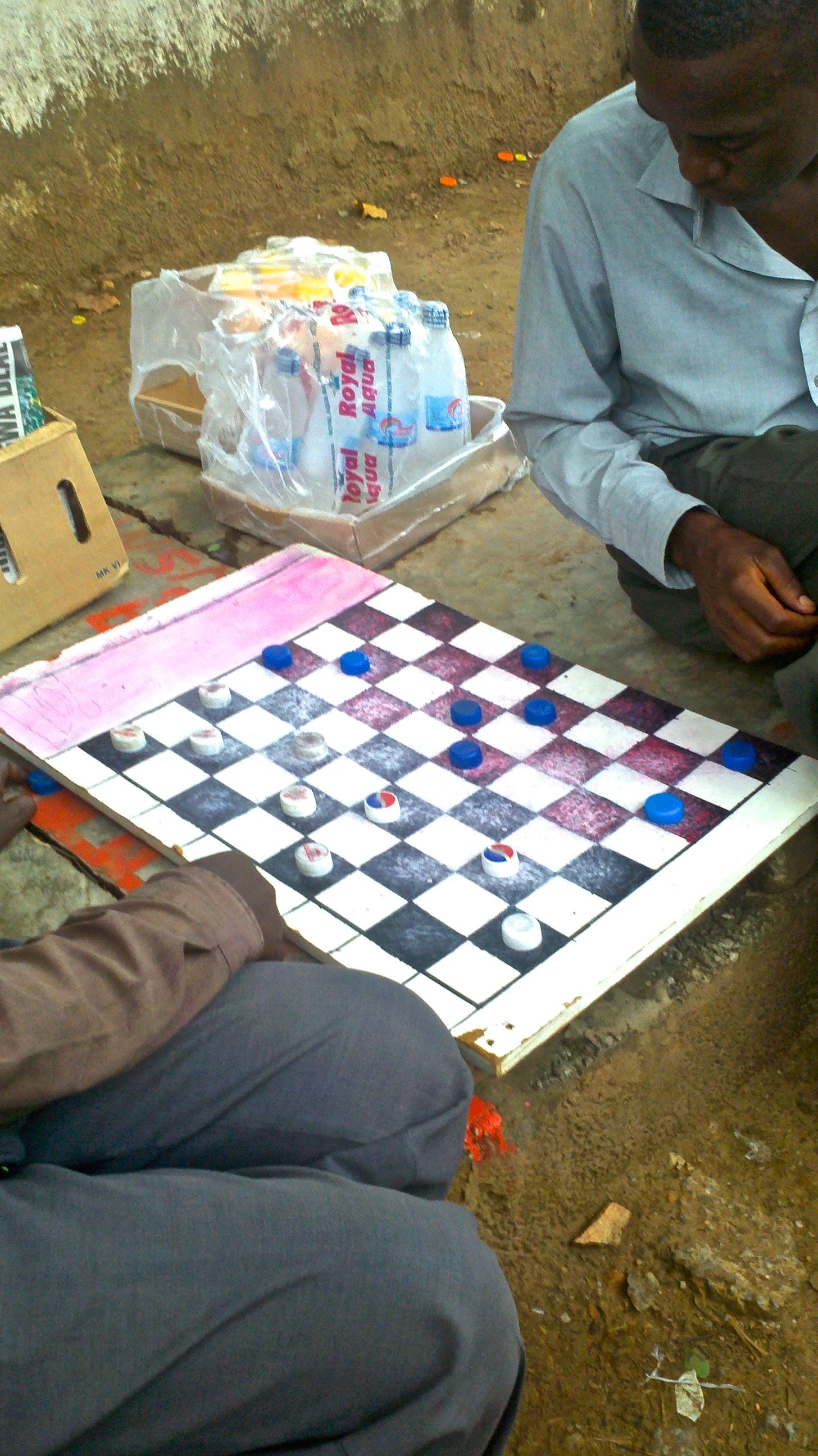 Men play checkers with Pepsi bottlecaps in Lusaka, the capital of Zambia. Image by Jina Moore. Zambia, 2014.