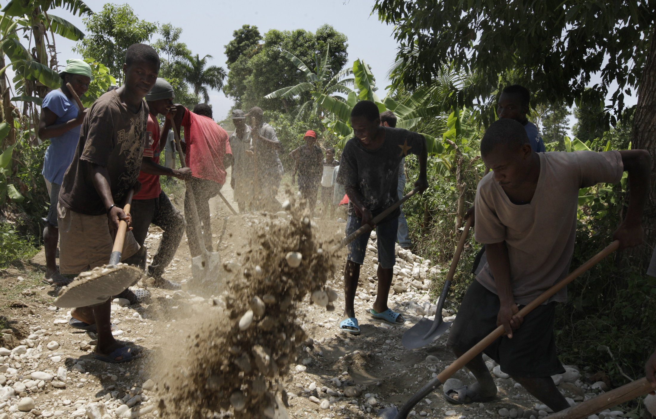 Residents of the village of Lot Bo Ladig spread gravel to patch a rutted road to their town. The gravel was purchased by Community Health Initiative so that a heavy truck with a well-drilling rig could make its way to the village. Image by Mary Chind. Haiti, 2013.