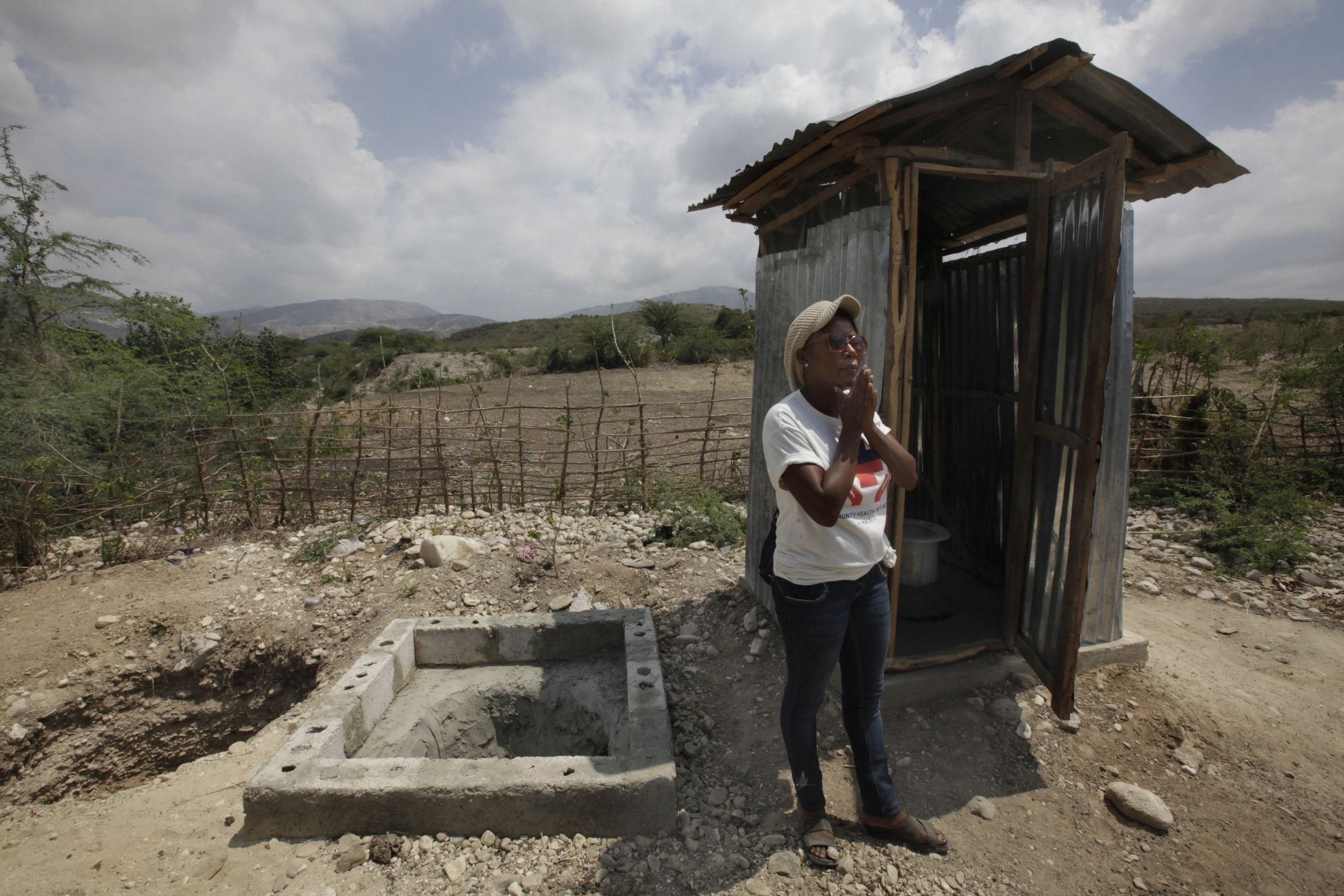 Public health worker Tamarra Joseph stands by a latrine that villagers built with help from the Community Health Initiative. When the latrine is full, the structure will be moved to the neighboring pit. The filled pit will be covered, and its contents will be composted for eventual use as fertilizer. Image by Mary Chind. Haiti, 2013. Media file: tamarra_joseph.jpg
