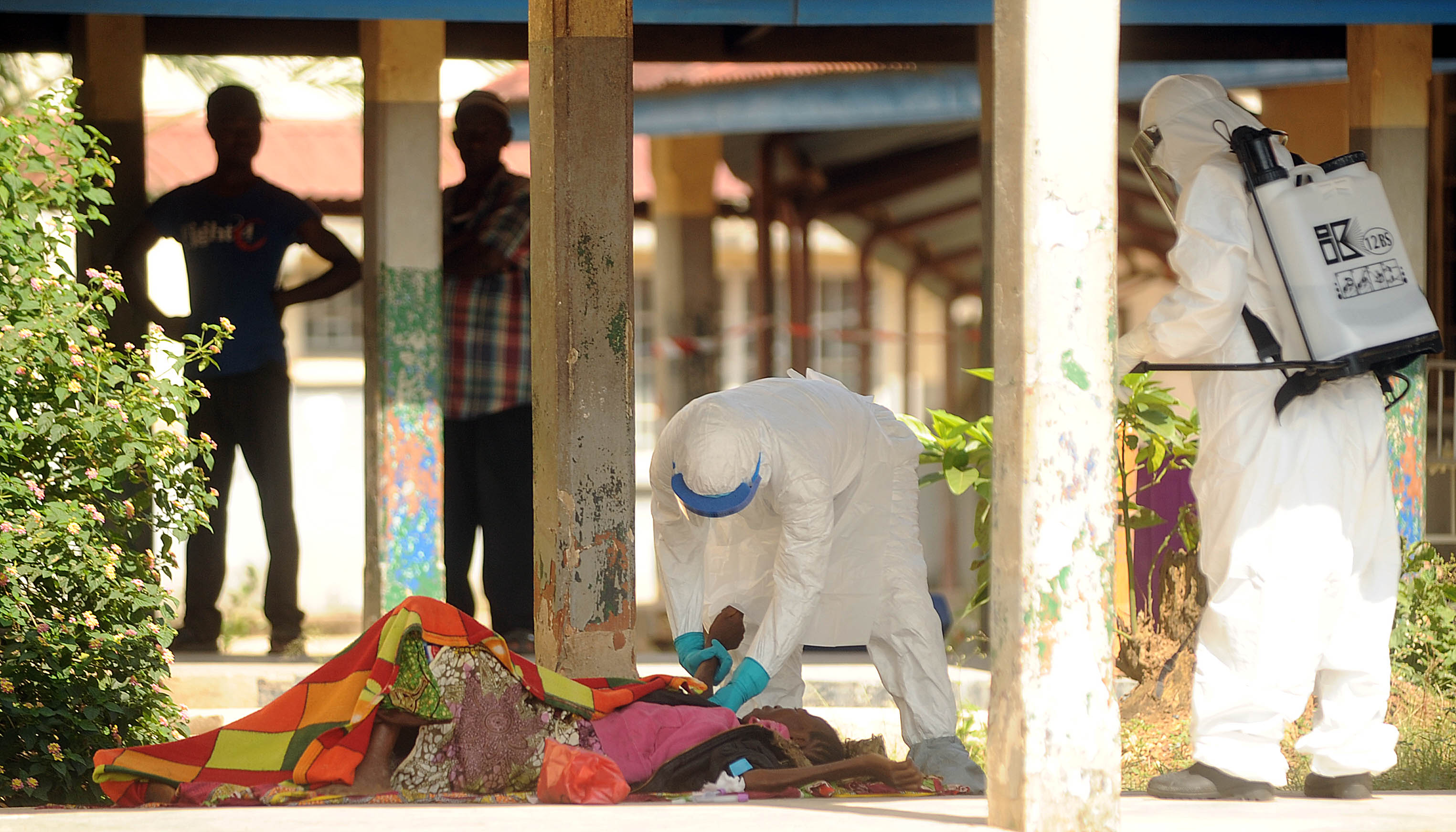 Healthcare workers at Kono Government Hospital tend to a suspected Ebola victim on the walkway that connects two hospital buildings as people freely walk around the medical facility in Koidu City, Kono District, Sierra Leone on Dec. 10, 2014. Image by Michael G. Seamans. Sierra Leone, 2015. Media file: sierra_leone_health_care_valley_news_003.jpg