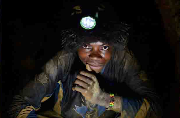 A young miner shines his headlamp underground in the mine where he scours for tin ore. Image by Fiona Lloyd-Davies. DRC, 2013.