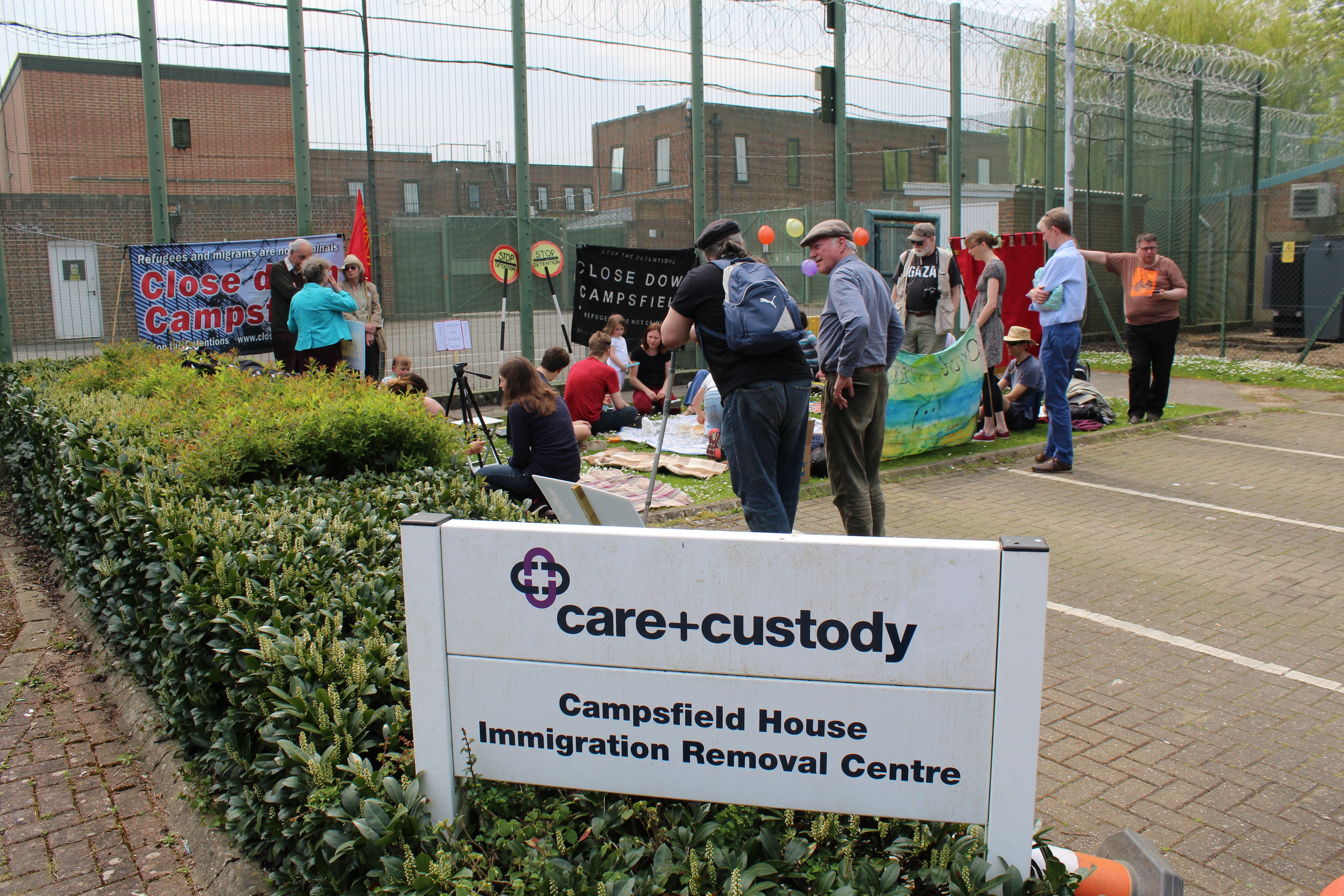 Protestors gather outside the detention center, which is run by Mitie, a private corporation. They object to what they consider exploitative practices by Mitie and the fact that migrants can be detained without judicial oversight. Image by Abe Kenmore. United Kingdom, 2016. Media file: img_0879.jpg