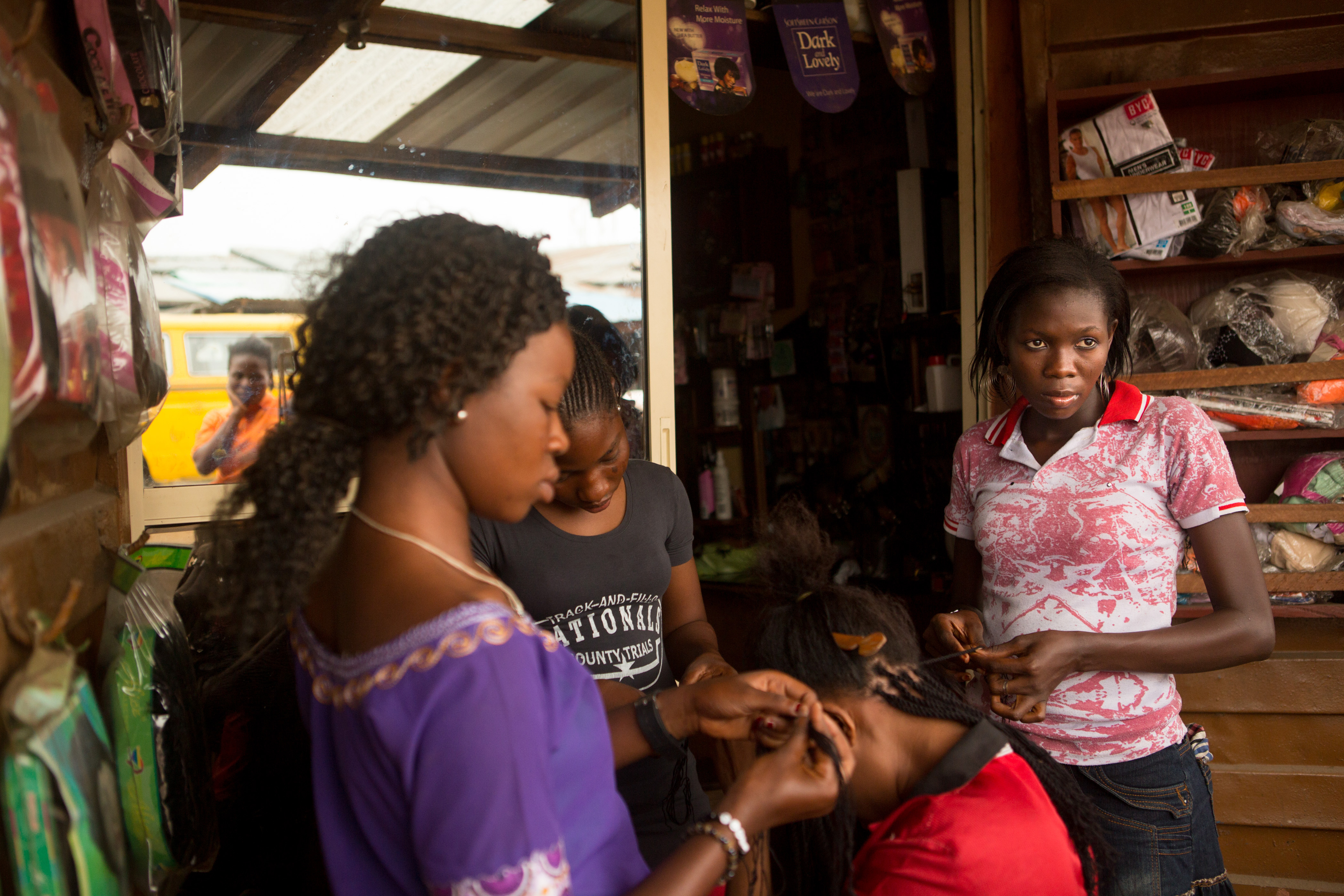 In Lagos, Nigeria, "Morayo" (assumed name), right, 21, braids hair at the salon where she is part of an 18-month-long vocational program. At the end of the program, participants are given equipment of their own so that they might start their own business. Morayo had an abortion several years ago at a local clinic but has not told anyone other than her sister. Image by Allison Shelley. Nigeria, 2013. Media file: pulitzer_globalpost_002.jpg