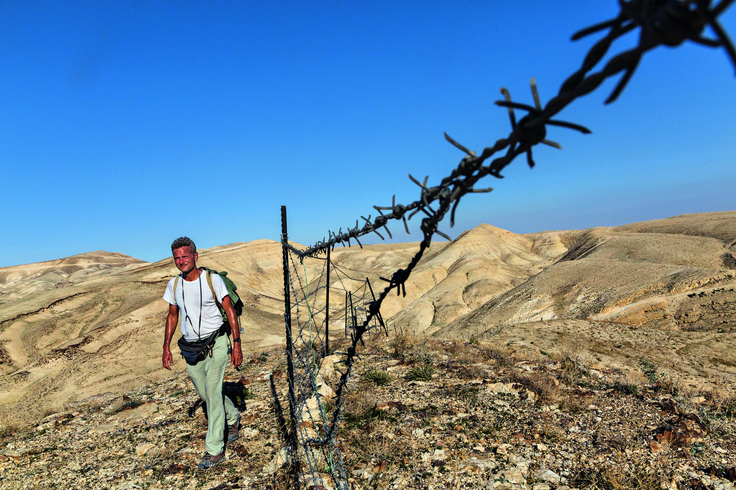 Striding toward Bethlehem, in the West Bank, Salopek is detoured by a herder’s tattered fence, one of the first human-made barriers—other than checkpoints and border gates—he’s faced in some 2,300 miles since he started out in Ethiopia. Image by John Stanmeyer/National Geographic. Media file: bethlehem-salopek.jpg