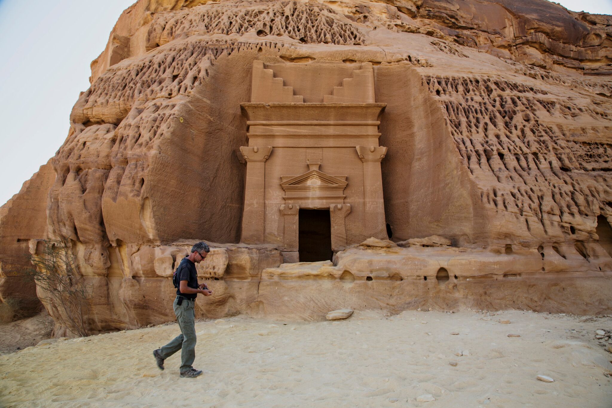 Paul Salopek wanders through the ancient Nabataean ruins of Madain Salih, carved into sandstone outcrops some 2,000 years ago. These structures were used as tombs for the wealthy during the Nabataean era. The kingdom stretched from its capital Petra in Jordan south to Madain Salih in the Hejaz region of present-day Saudi Arabia. Photo shows a tomb façade in the Al Khuraymat area of Madain Salih. Image by John Stanmeyer/National Geographic. Media file: nabataean-ruins-salopek.jpg
