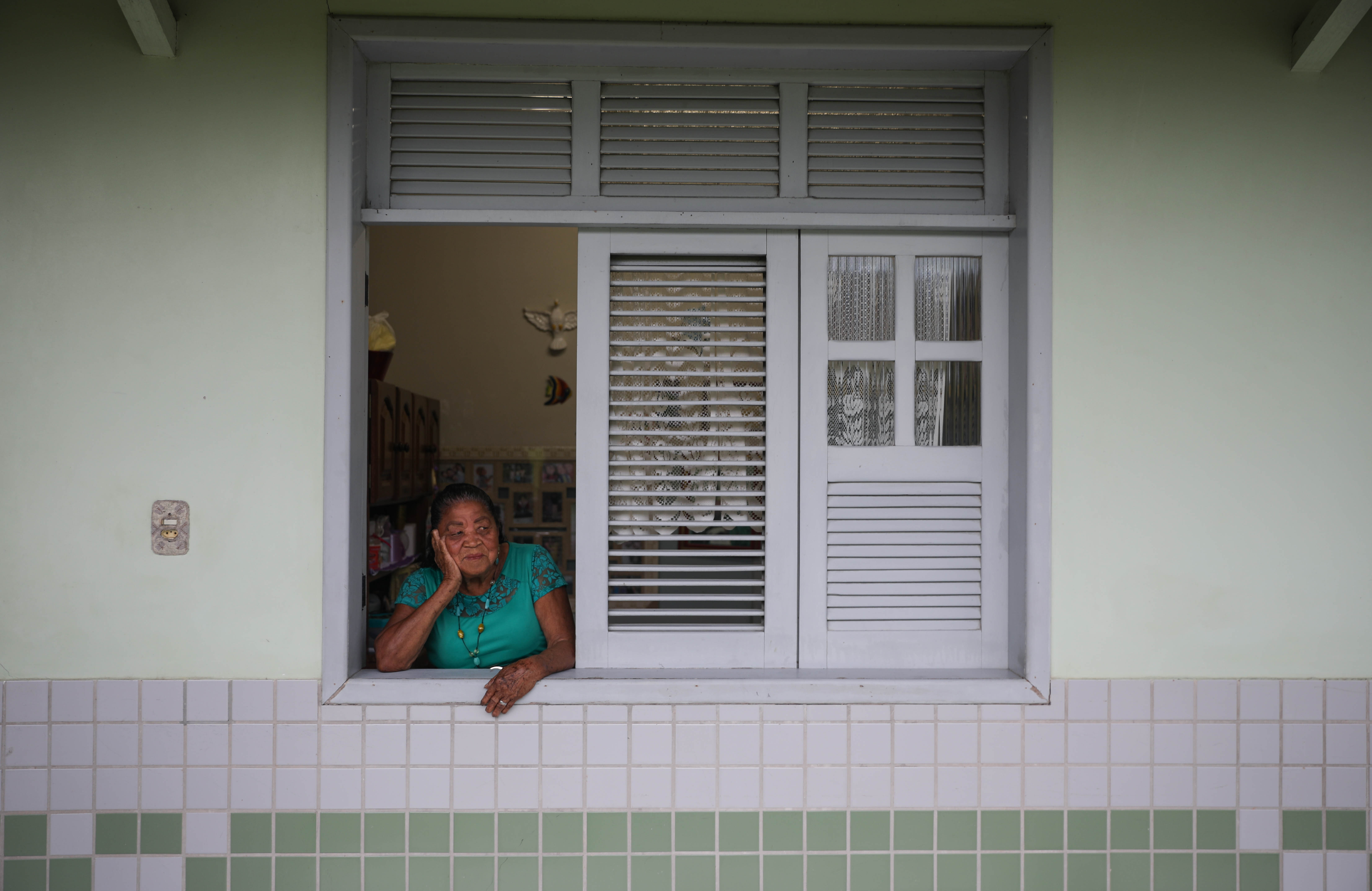 Maria da Silva Trindade peeks out of her living room window to chat with the other residents of Marituba’s former leprosy colony. Trindade was diagnosed with the disease at the age of 15, and she moved into the colony the same year. Nearly 80 years later she’s still there. Image by Anton L. Delgado. Brazil, 2020. Maria da Silva Trindade peeks out of her living room window to chat with the other residents of Marituba’s former leprosy colony. Trindade was diagnosed with the disease at the age of 15, and she moved into the colony the same year. Nearly 80 years later she’s still there. Image by Anton L. Delgado. Brazil, 2020.