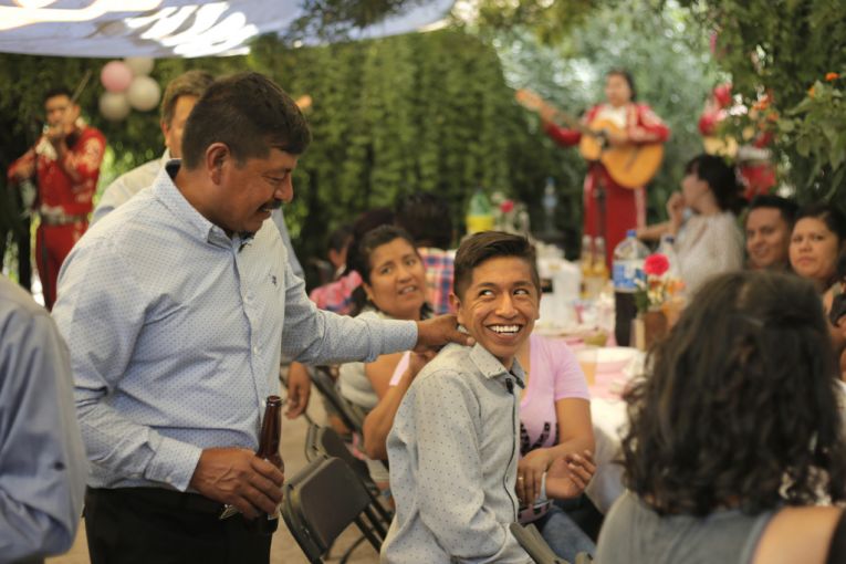 Winny Contreras laughs with his son Ricardo as a mariachi band plays at his eldest daughter's graduation party in their home in Mexico. Image by Ingrid Holmquist. Mexico, 2018. Winny Contreras laughs with his son Ricardo as a mariachi band plays at his eldest daughter's graduation party in their home in Mexico. Image by Ingrid Holmquist. Mexico, 2018.