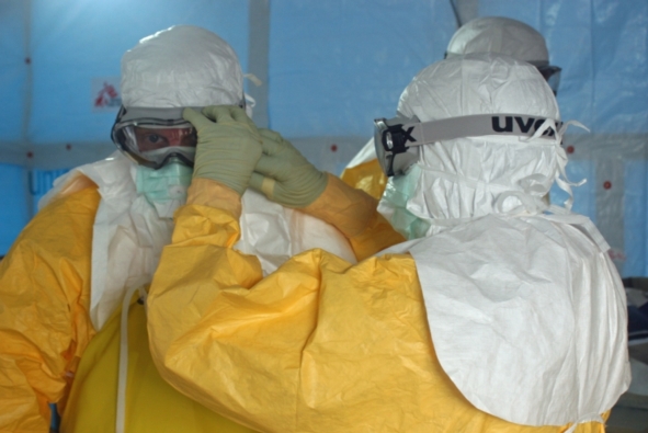 A Médecins Sans Frontières/Doctors Without Borders (MSF) staff member ties the face mask of Dr. Jordan Tappero, CDC, before Dr. Tappero enters an Ebola treatment unit. Image by CDC Global/Flickr, CC BY 2.0.