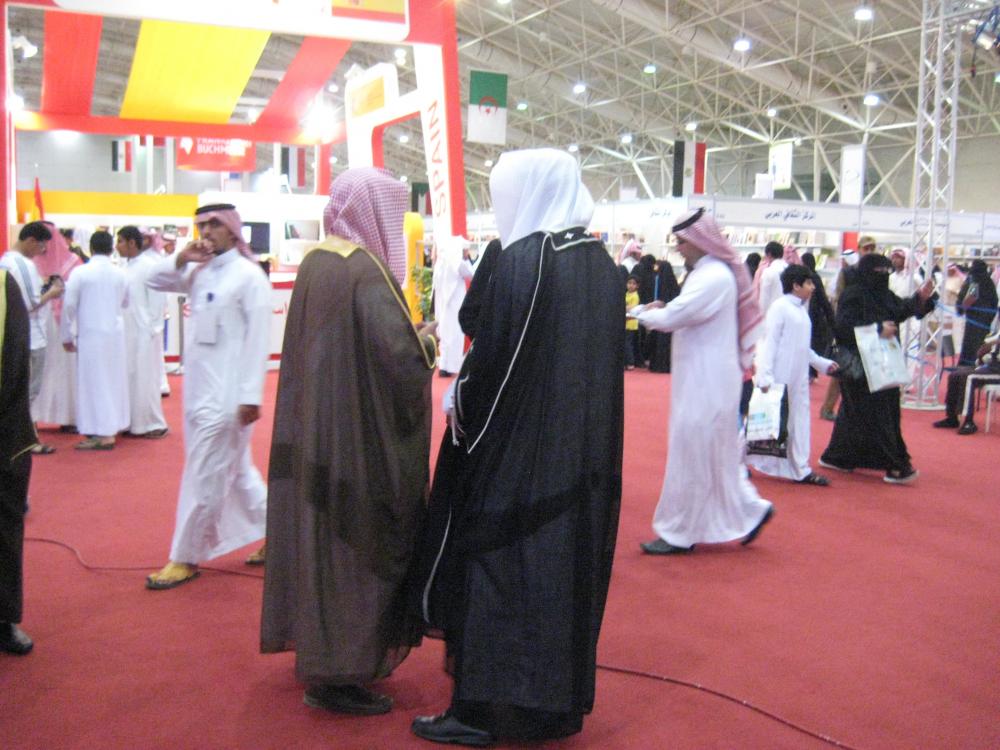 Two religious policemen on patrol at Riyadh's International Book Fair. Although the strict interpretation of Islam prevalent in Saudi Arabia, Wahhabism, frowns upon fancy dress as an impious pretension, the religious police often wear the formal robe, the bisht, as seen here. Image by Caryle Murphy. Riyadh, 2014. Media file: muttawa_or_religious_police_at_the_book_fair.jpg