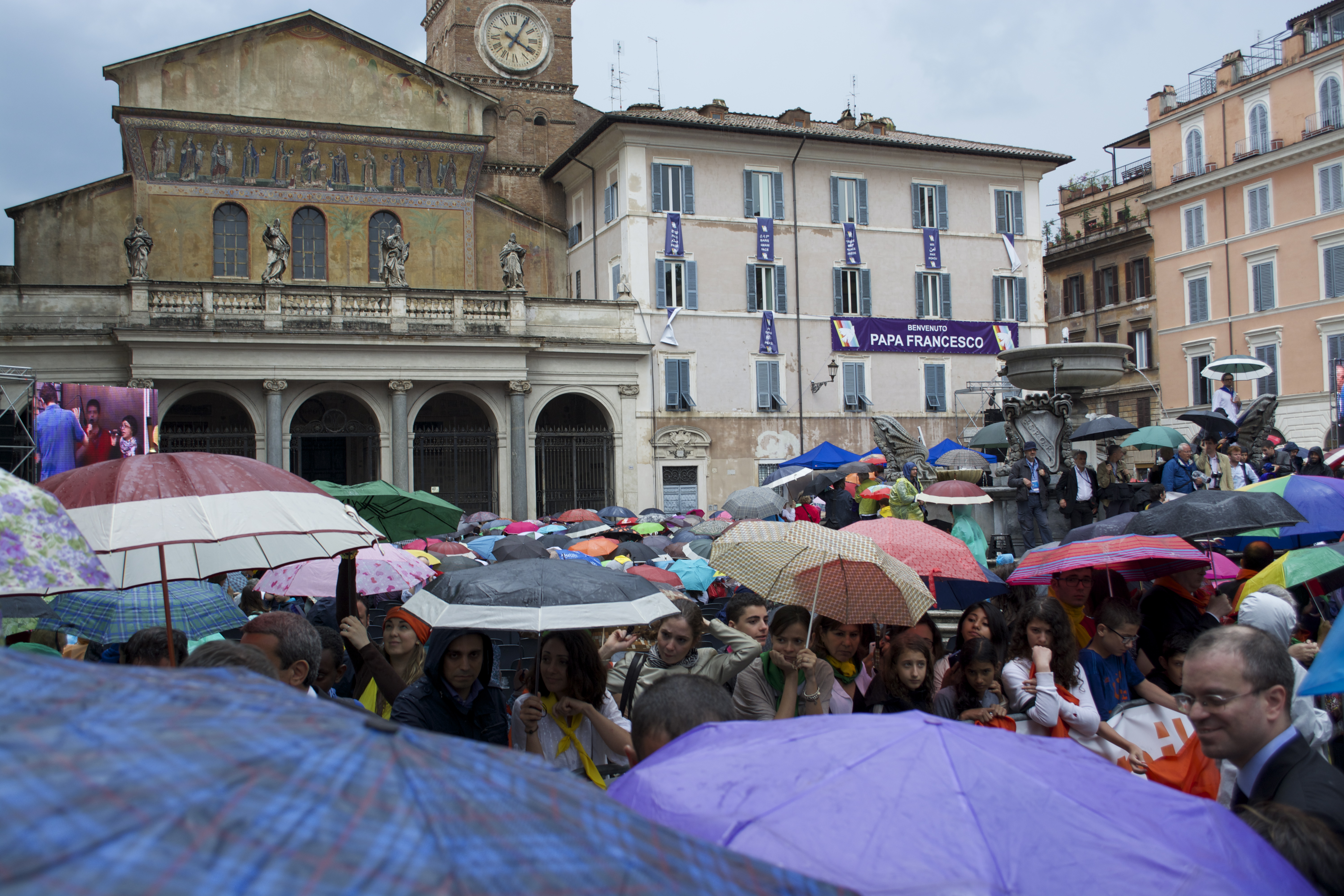 Thousands braved inclement weather and gathered in the square outside the Basilica di Santa Maria in Trastevere to await the arrival of the pope. Image by Molly K. Dutmers. Italy, 2014.