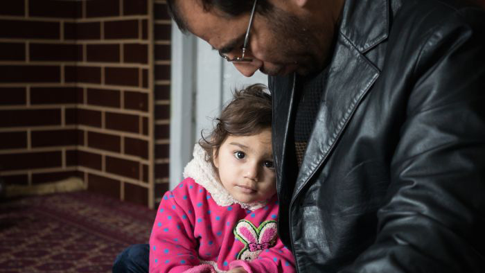 Dr. Wahid Qaderi holds his daughter in his home in Kabul, Afghanistan. His wife, mother, mother-in-law and five children recently crossed by boat from Turkey to Greece, while he stayed behind to try and sell their home. Image by Alexandria Bombach. Afghanistan, 2016.