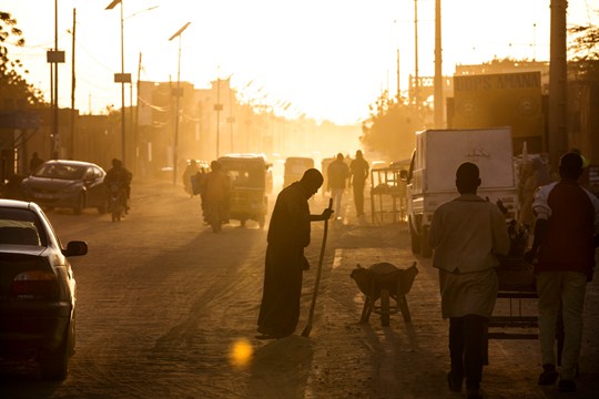 A man sweeps dust off the street at dusk in Agadez, Niger. Image by Joe Penney. Niger, 2018. A man sweeps dust off the street at dusk in Agadez, Niger. Image by Joe Penney. Niger, 2018.