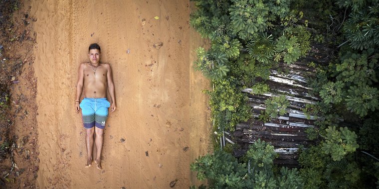 Ednei poses on the tracks left by the trucks used to transport wood that pass through the borders of his territory. Right: what's left of 26 trees destroyed by illegal lumberjacks in indigenous Maró territory. Image by Pablo Albarenga. Brazil, 2019. Ednei poses on the tracks left by the trucks used to transport wood that pass through the borders of his territory. Right: what's left of 26 trees destroyed by illegal lumberjacks in indigenous Maró territory. Image by Pablo Albarenga. Brazil, 2019.