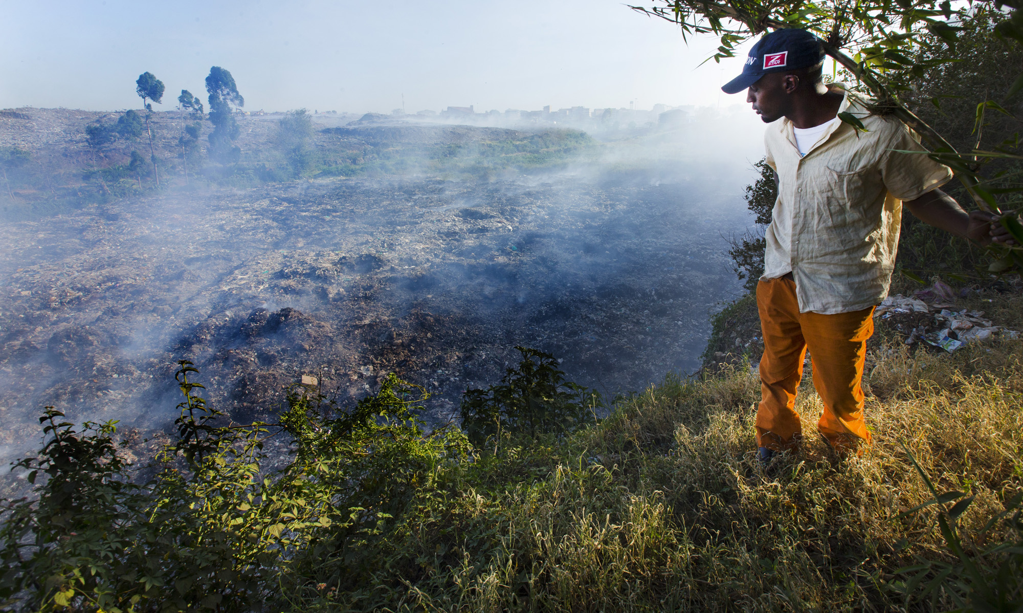 A man stands on the edge of a precipice overlooking Dandora, Korogocho’s 30-acre massive dump of smoldering garbage. People scavenge through the dump looking for anything of value. Image by Mark Hoffman. Kenya, 2017. A man stands on the edge of a precipice overlooking Dandora, Korogocho’s 30-acre massive dump of smoldering garbage. People scavenge through the dump looking for anything of value. Image by Mark Hoffman. Kenya, 2017.