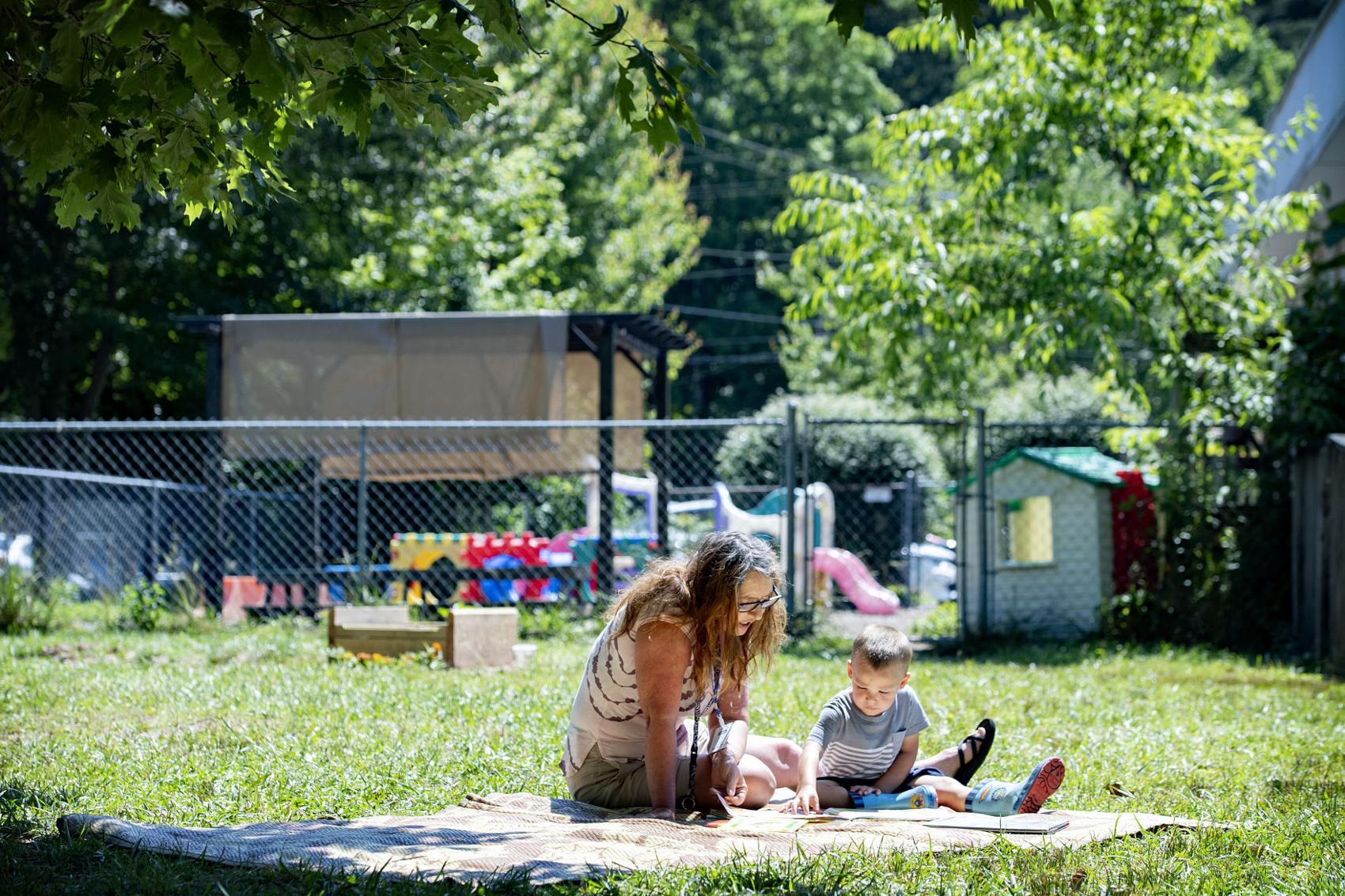 Bell’s School teacher Angela Mehaffey reads a book with Elliot Fink, 2, on a blanket outside the Fletcher preschool June 22. Image by Angeli Wright/Asheville Citizen Times/North Carolina News Collaborative. United States, 2020. Bell’s School teacher Angela Mehaffey reads a book with Elliot Fink, 2, on a blanket outside the Fletcher preschool June 22. Image by Angeli Wright/Asheville Citizen Times/North Carolina News Collaborative. United States, 2020.