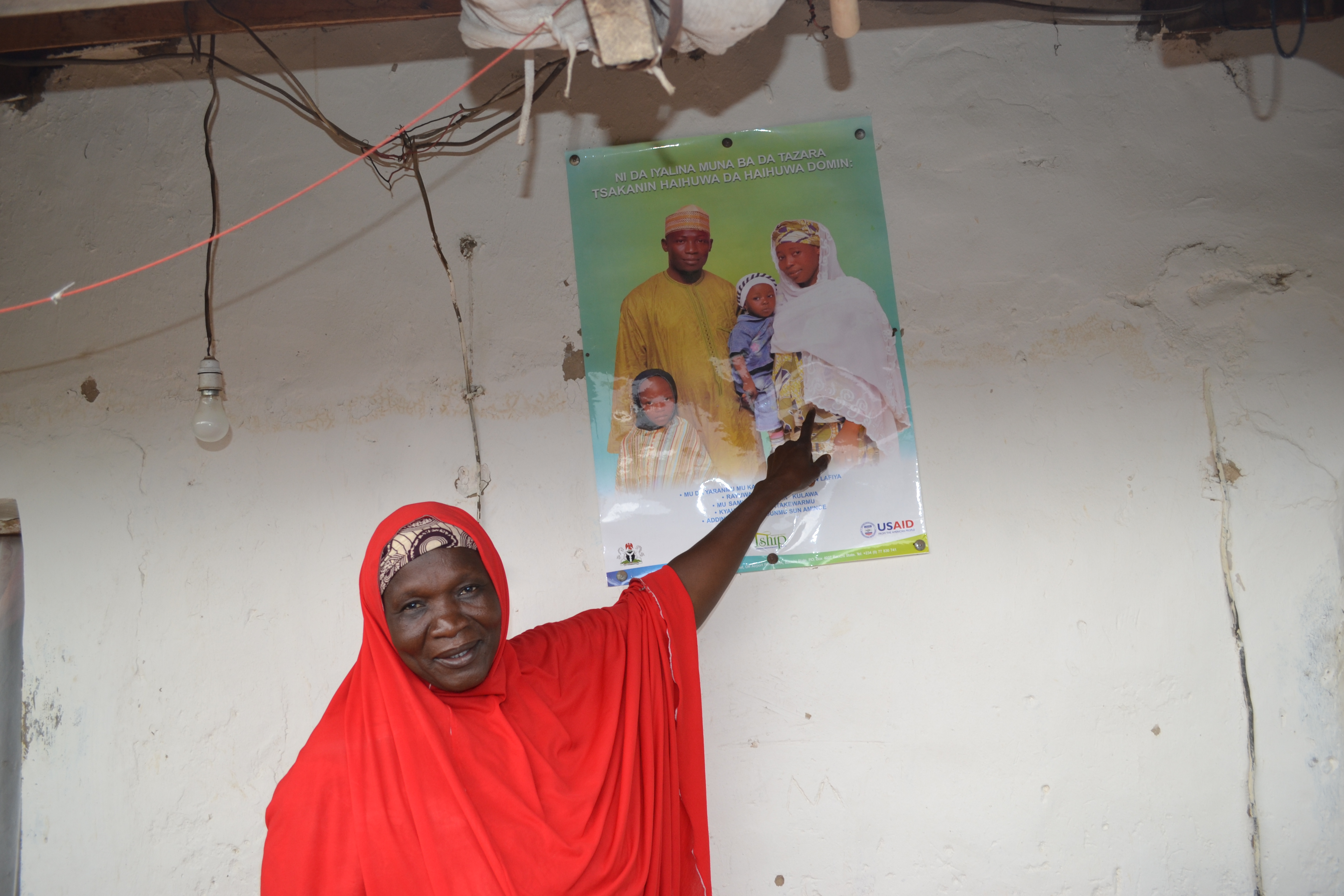 Mama Mubarak 50, an unpaid volunteer points to a poster in Hausa that says “My family and I do family-planning.” The acceptance and use of family planning in Bauchi state is just 2 percent. Childbearing begins early and births are closely spaced. Image by Ameto Akpe. Nigeria, 2013. Media file: mama_mubarak.jpg