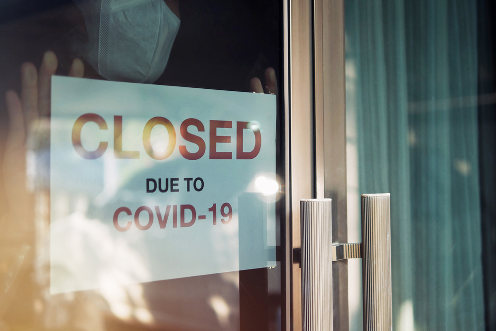 Business office or store shop is closed, bankrupt business due to the effect of novel Coronavirus (COVID-19) pandemic. Unidentified person wearing mask hanging closed sign in background on front door. Image by Chansom Pantip. Thailand, 2020. Business office or store shop is closed, bankrupt business due to the effect of novel Coronavirus (COVID-19) pandemic. Unidentified person wearing mask hanging closed sign in background on front door. Image by Chansom Pantip. Thailand, 2020.