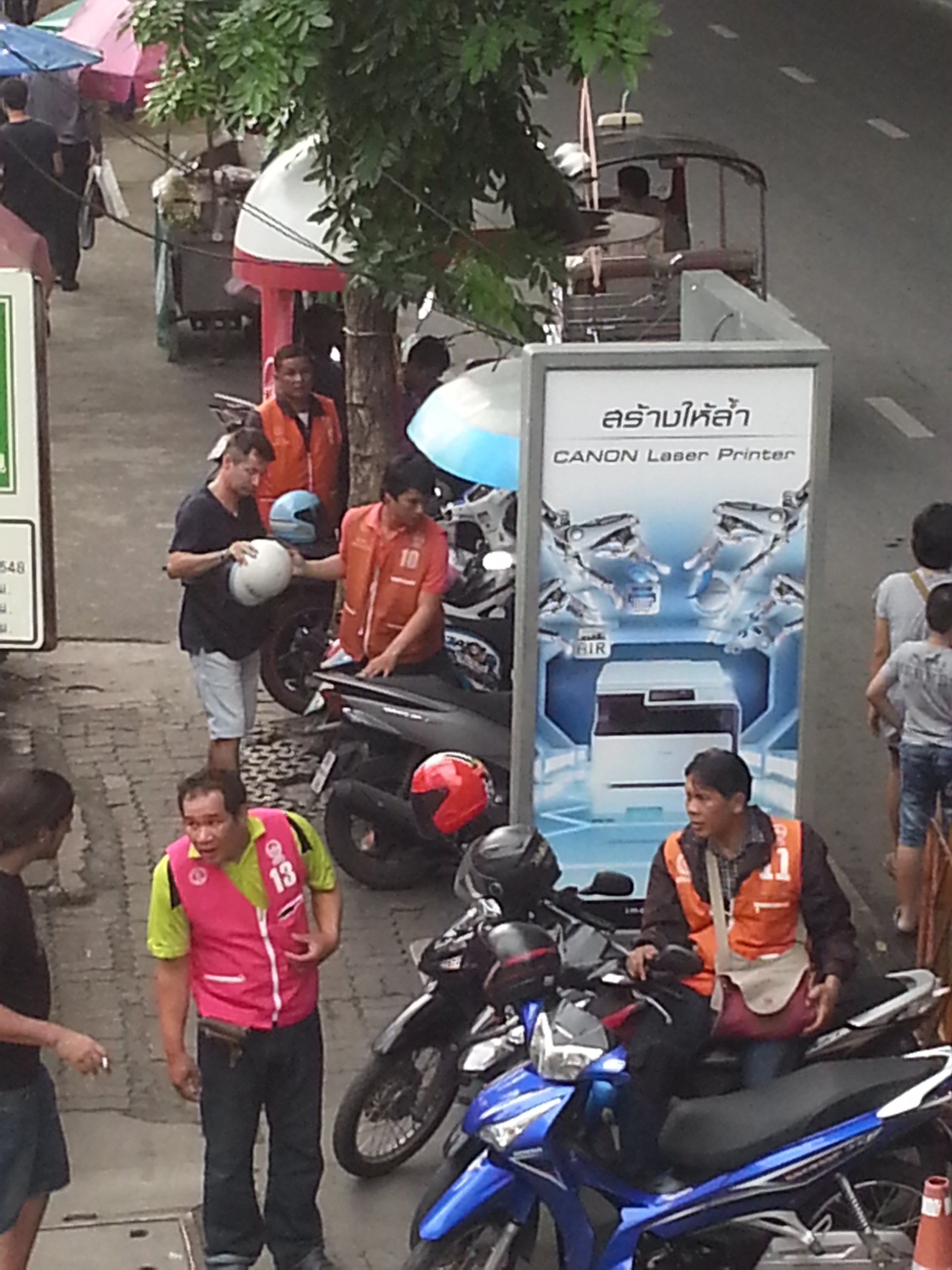 Motorcycle taxi drivers, in colored vests, wait for customers in Bangkok. Image by Tom Hundley. Thailand, 2014. Media file: tommototaxi2.jpg
