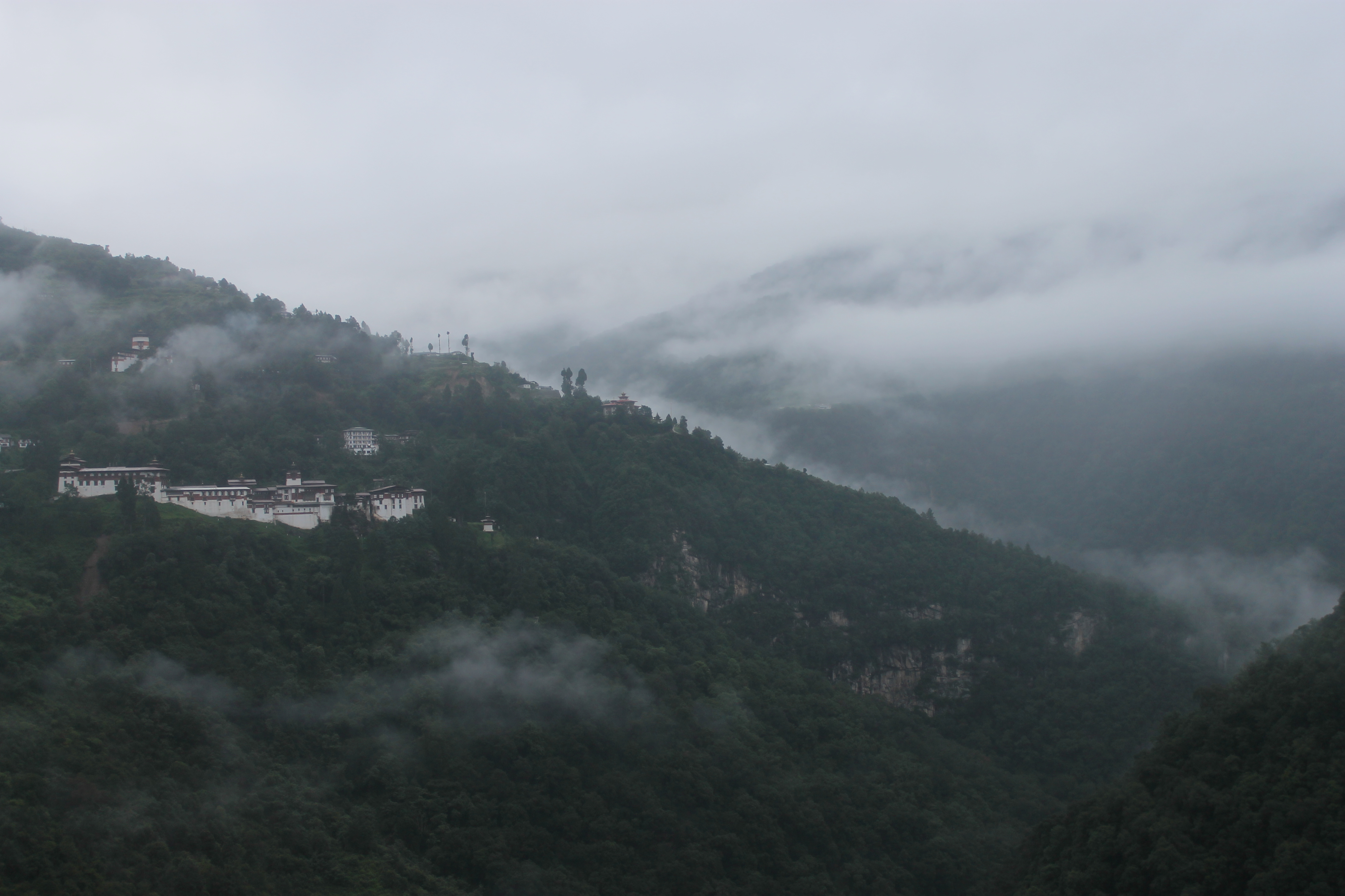 The Trongsa Dzong, or fortress, sits nestled among the trees in the early morning mist in the district of Trongsa. Image by Emma Johnson. Bhutan, 2019. The Trongsa Dzong, or fortress, sits nestled among the trees in the early morning mist in the district of Trongsa. Image by Emma Johnson. Bhutan, 2019.