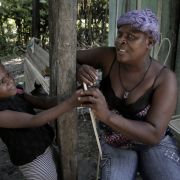 Belange, Haiti—August 3, 2018—Paula Paul (right) with her daughter, six year-old Marie Stacy (left) in front of their home in Belange, Haiti. Paula Paul has been diagnosed with cervical cancer. She has been undergoing treatment for the disease but due to lack of funds, has been thinking about not making the trips to the hospital in Mirebalais where she gets her chemotherapy. Image by José Antonio Iglesias. Haiti, 2018. Belange, Haiti—August 3, 2018—Paula Paul (right) with her daughter, six year-old Marie Stacy (left) in front of their home in Belange, Haiti. Paula Paul has been diagnosed with cervical cancer. She has been undergoing treatment for the disease but due to lack of funds, has been thinking about not making the trips to the hospital in Mirebalais where she gets her chemotherapy. Image by José Antonio Iglesias. Haiti, 2018.