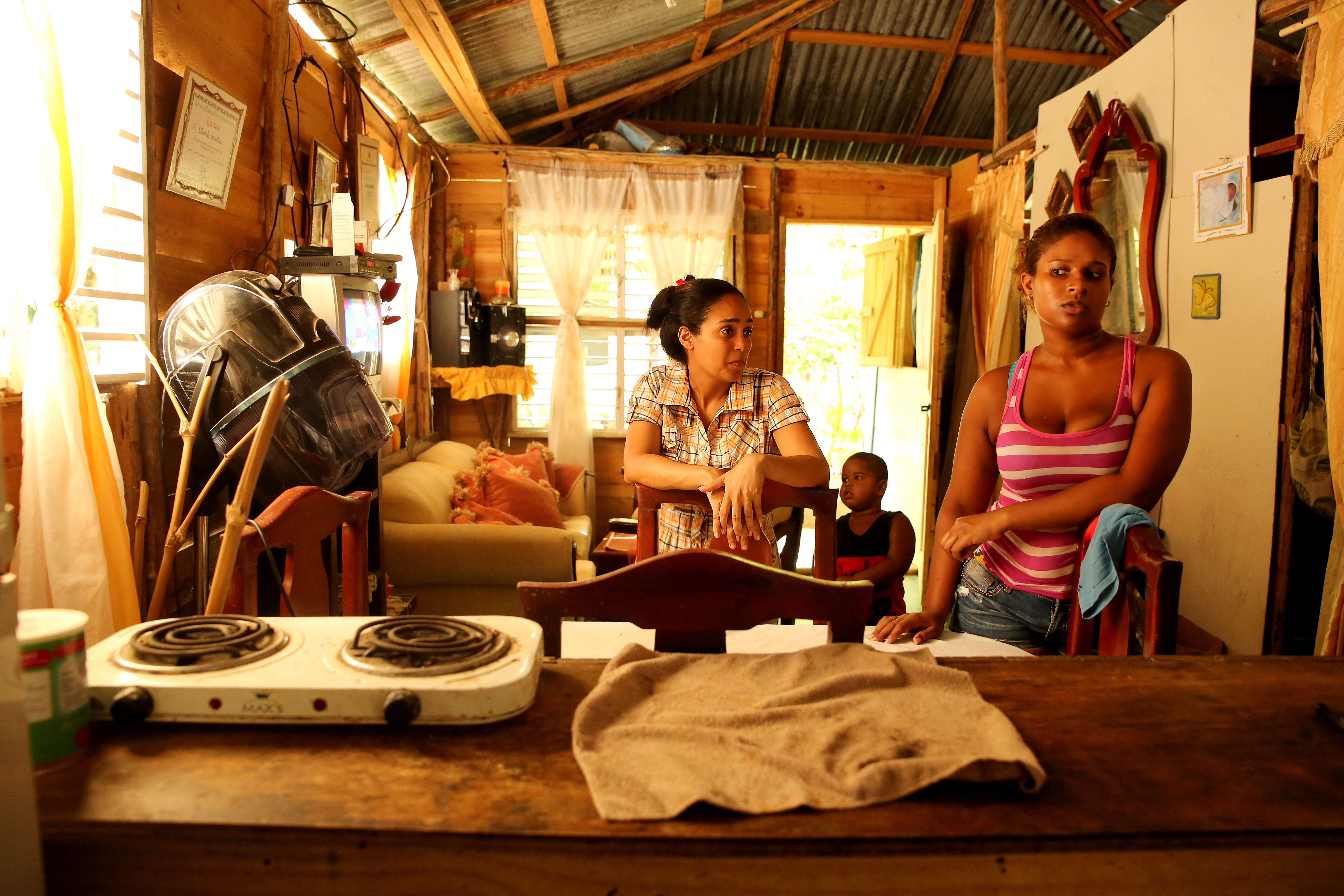 Magaly Lantigua and Nelly Sanchez discuss the costs of cooking with propane gas and electric stoves. Sanchez says she saves money using the electric stove on the counter, but both she and Lantigua agree the cost of cooking takes a majority of their families’ incomes. Lantigua uses gas as her most common cooking method. Image by Makenzie Huber. Dominican Republic, 2016. cost of cooking with propane gas and electric stoves