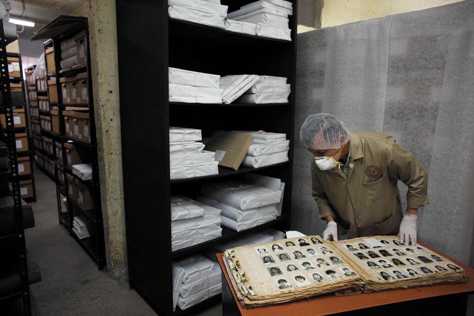 Wearing a mask and gloves to protect fragile documents, an archivist opens one of the thousands of books of photographs held by the Historical Archives of the National Police. The Guatemalans pictured inside were all detained or arrested by the National Police during the country’s long civil war. Many of their fates remain unknown. Sometimes, visitors to the archive—or the archivists themselves—will turn a page and recognize a friend or relative not seen in decades. Image by Lynn Johnson. Guatemala, 2017. Wearing a mask and gloves to protect fragile documents, an archivist opens one of the thousands of books of photographs held by the Historical Archives of the National Police. The Guatemalans pictured inside were all detained or arrested by the National Police during the country’s long civil war. Many of their fates remain unknown. Sometimes, visitors to the archive—or the archivists themselves—will turn a page and recognize a friend or relative not seen in decades. Image by Lynn Johnson. Guatemala, 2017.