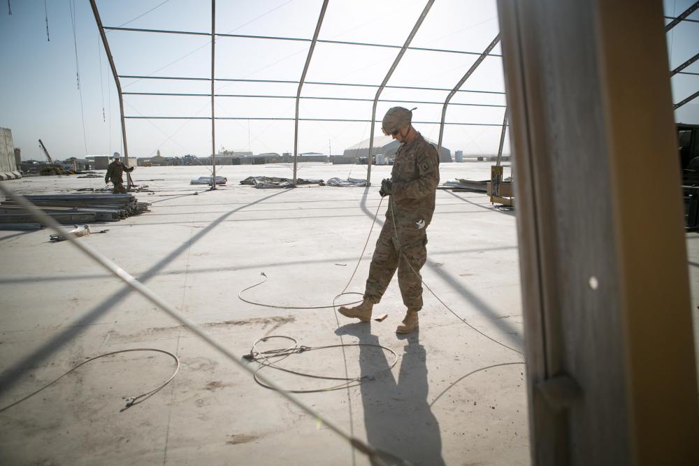 Spc. Nate Hitchcock wipes the sweat from his eyes while standing on a pile of beams that formerly held up a maintenance tent for military helicopters. Image by Meghan Dhaliwal. Afghanistan, 2014. Media file: afghanday_6of11.jpg