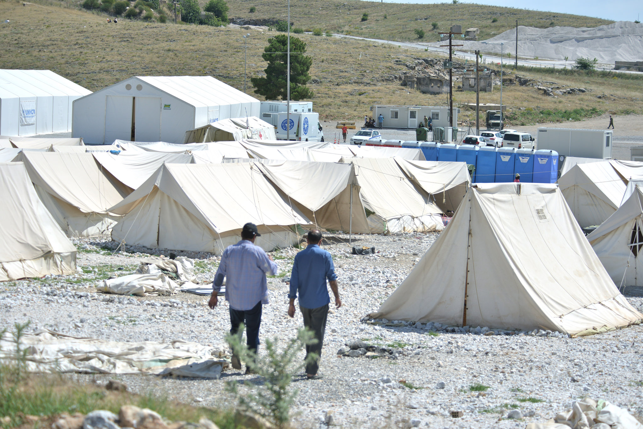 Refugees were evacuated to camps like this one, in Larisa, Greece. It is located on a fenced gravel lot dotted with tents, off the side of a divided highway lined by fields the color of sand, over three-hours drive from Athens in one of the hottest, driest parts of the country. More than 800 Afghans and Syrians were deposited here, in the middle of nowhere, by government busses, with no information on why or for how long. Image by Frederick Atax. Greece, 2016. Many were evacuated to camps like this one, in Larisa, Greece. It’s located on a fenced gravel lot dotted with tents, off the side of a divided highway lined by fields the color of sand, over three-hours drive from Athens in one of the hottest, driest parts of the country. More than 800 Afghans and Syrians were deposited here, in the middle of nowhere, by government busses months ago, with no information on why or for how long. Image by Frederick Atax.