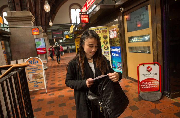 Au pair Lucila Espinosa Milay checks her receipt as she walks through a row of money transfer businesses after wiring part of her paycheck to siblings back in the Philippines, at Central Station in Copenhagen. Milay pays the school fees for several of her eight siblings back home, sending money every 15 days. Remittances are a huge economic driver in the Philippines. Image by Allison Shelley. Philippines, 2016. Au Pair