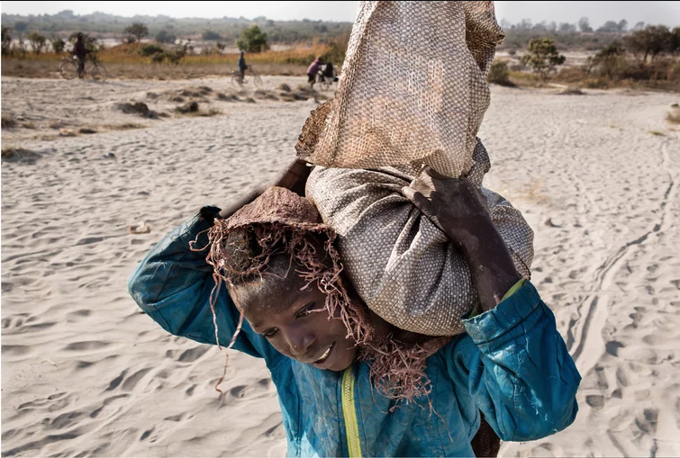 Daniel (11) carries a bag of cobalt on his back. He works in a mine ferrying sacks of cobalt to a depot. Image by Sebastian Meyer. Democratic Republic of Congo, 2018. Daniel (11) carries a bag of cobalt on his back. He works in a mine ferrying sacks of cobalt to a depot. Image by Sebastian Meyer. Democratic Republic of Congo, 2018.