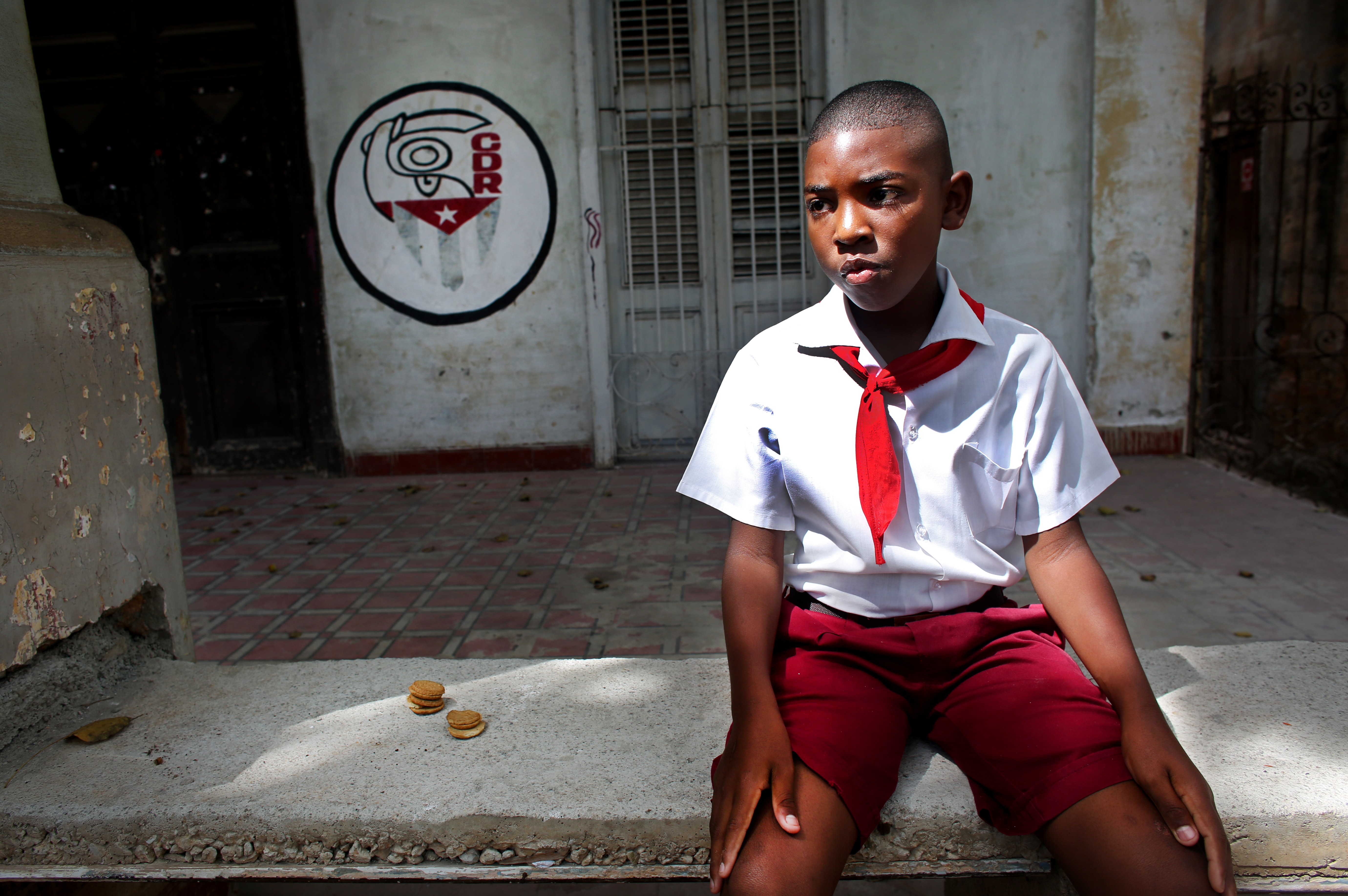 A young student wearing the uniform of communist youth rests in front of an office for the CDR (Comité de Defensa de la Revolución, or Committee for the Defense of the Revolution,) which is a network of neighborhood watch organizations reporting on any "counter-revolutionary" or anti-communist activity, in Havana, Cuba. Photo by: Yana Paskova
